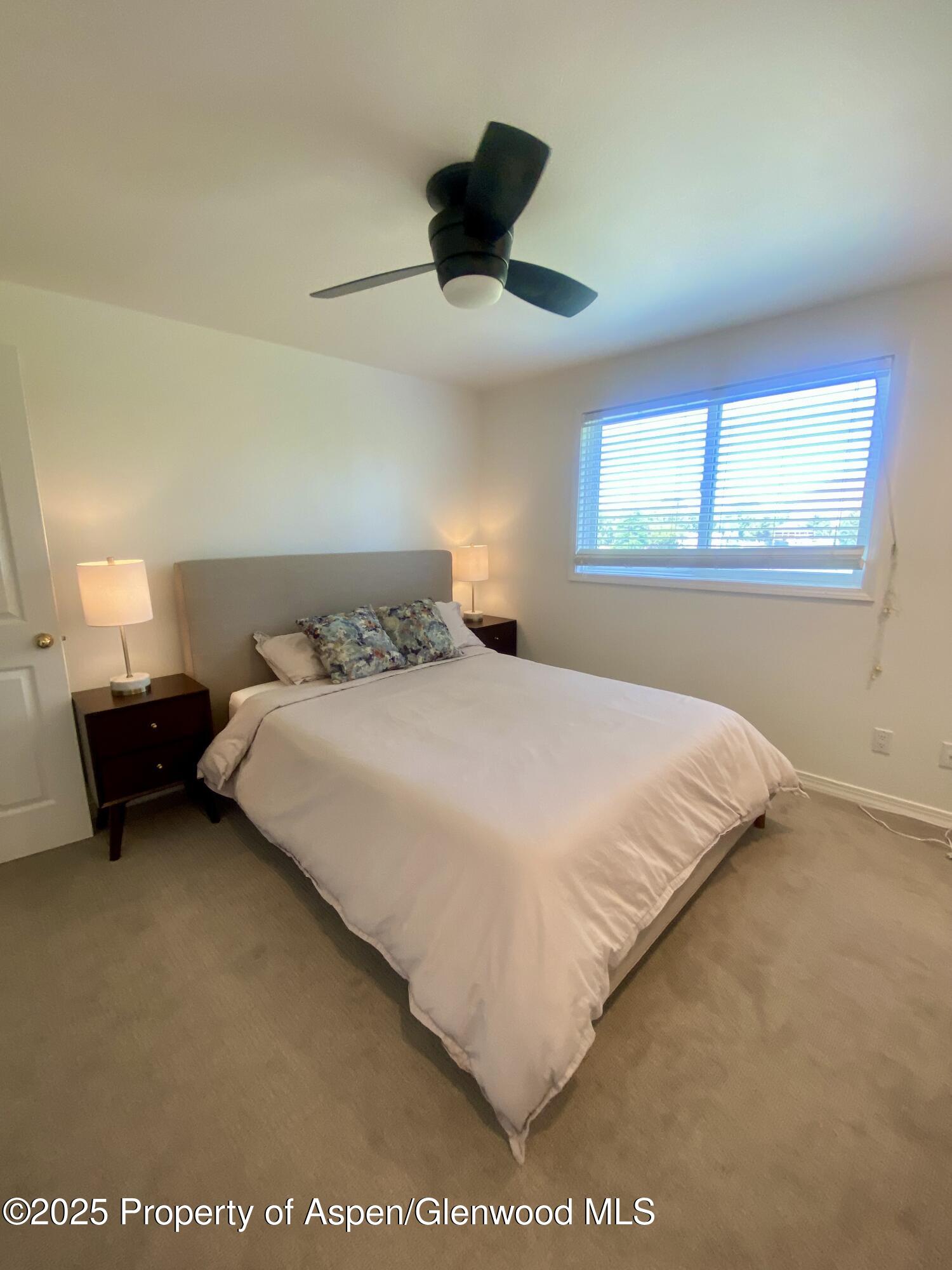 Furnished bedroom with a large bed, patterned pillows, matching bedside lamps, and a black ceiling fan.
