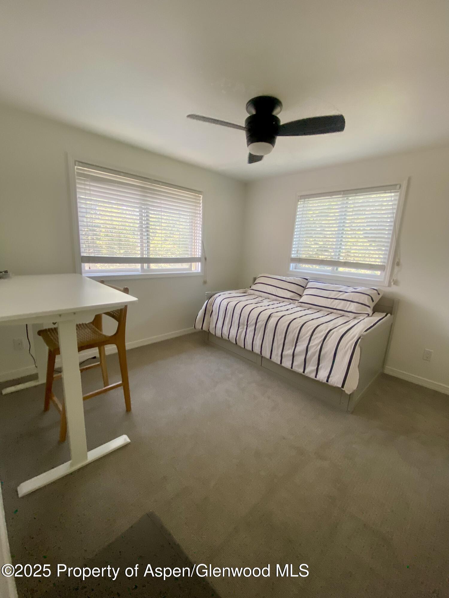 Bedroom with a striped bed beneath two windows and a black ceiling fan.