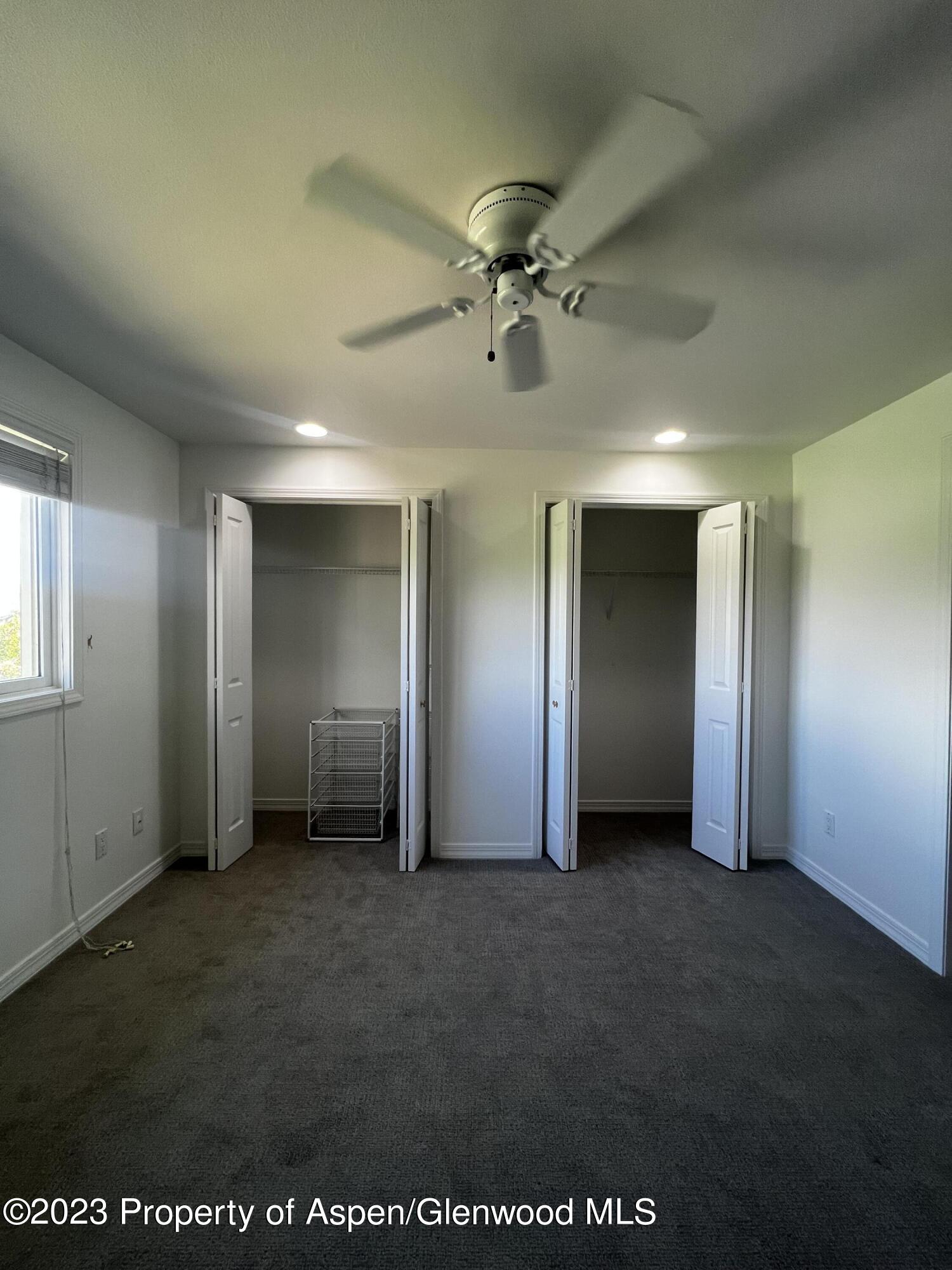 Unfurnished bedroom with two open closets, gray carpet, and a ceiling fan.