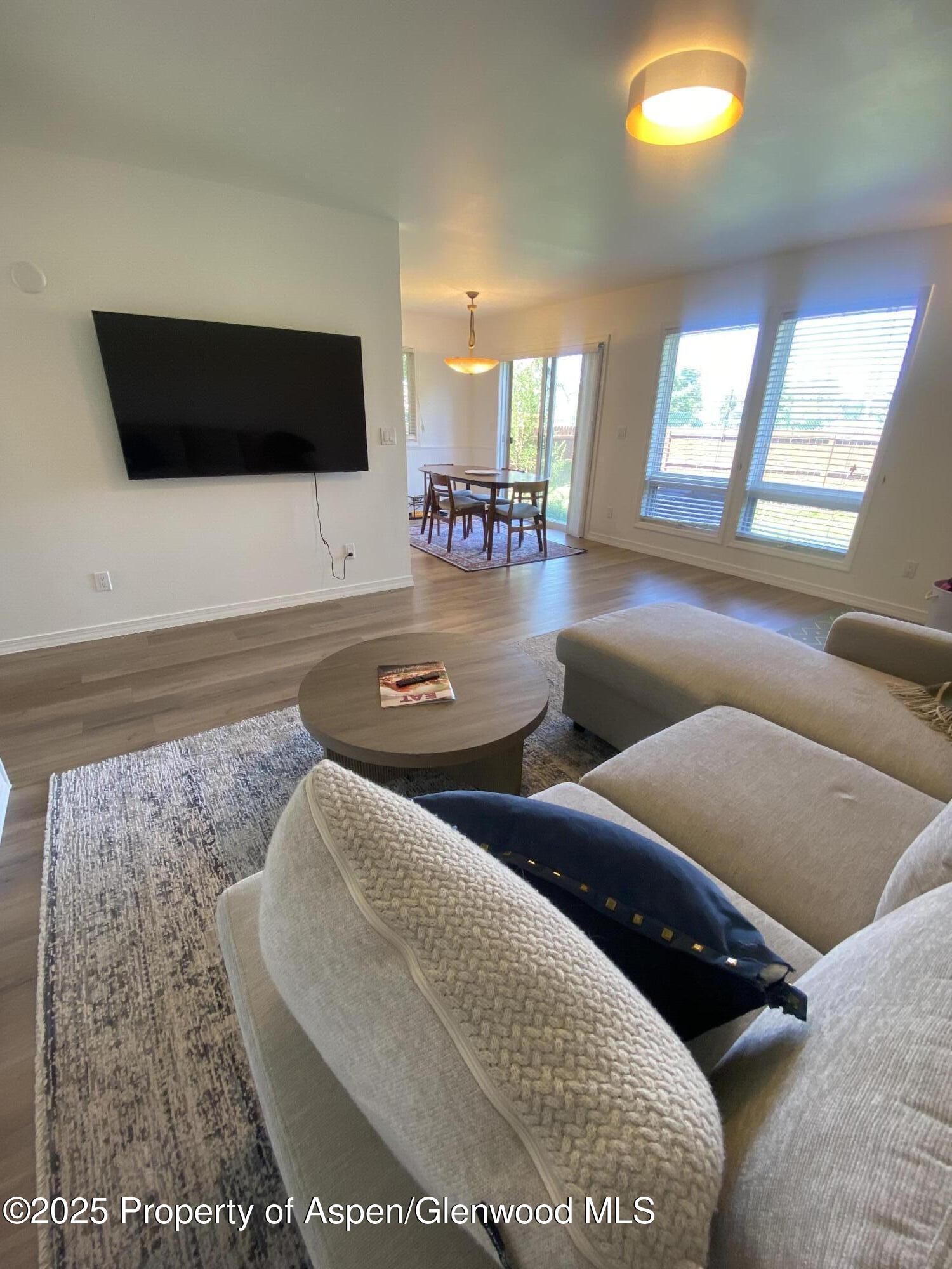 Furnished living room with a wall-mounted television, light sectional, and bright windows.