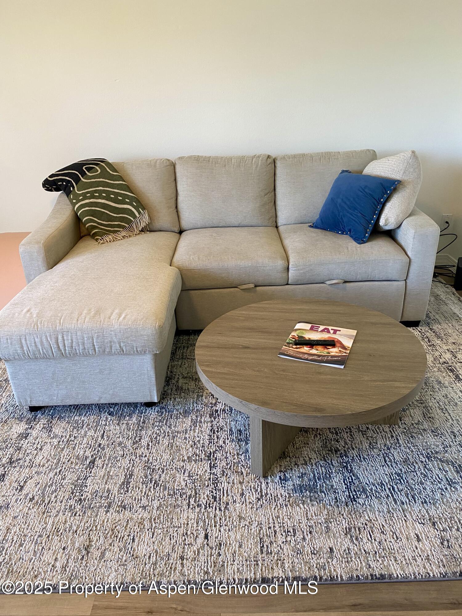 Living room with a gray sectional and chaise, round wood coffee table, and patterned rug.