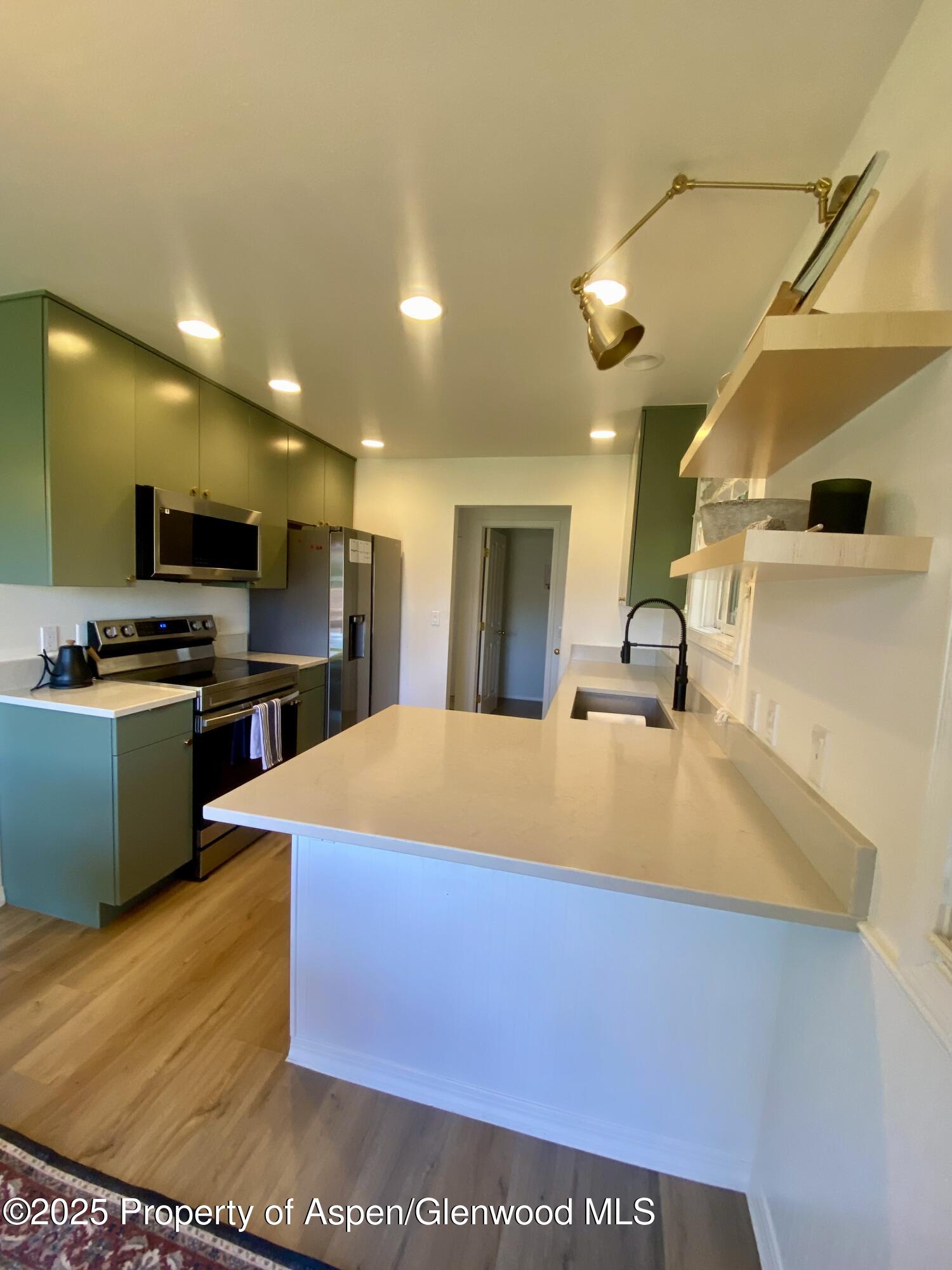 Modern kitchen with green cabinets, stainless appliances, a large white island, and a black spring-neck faucet.