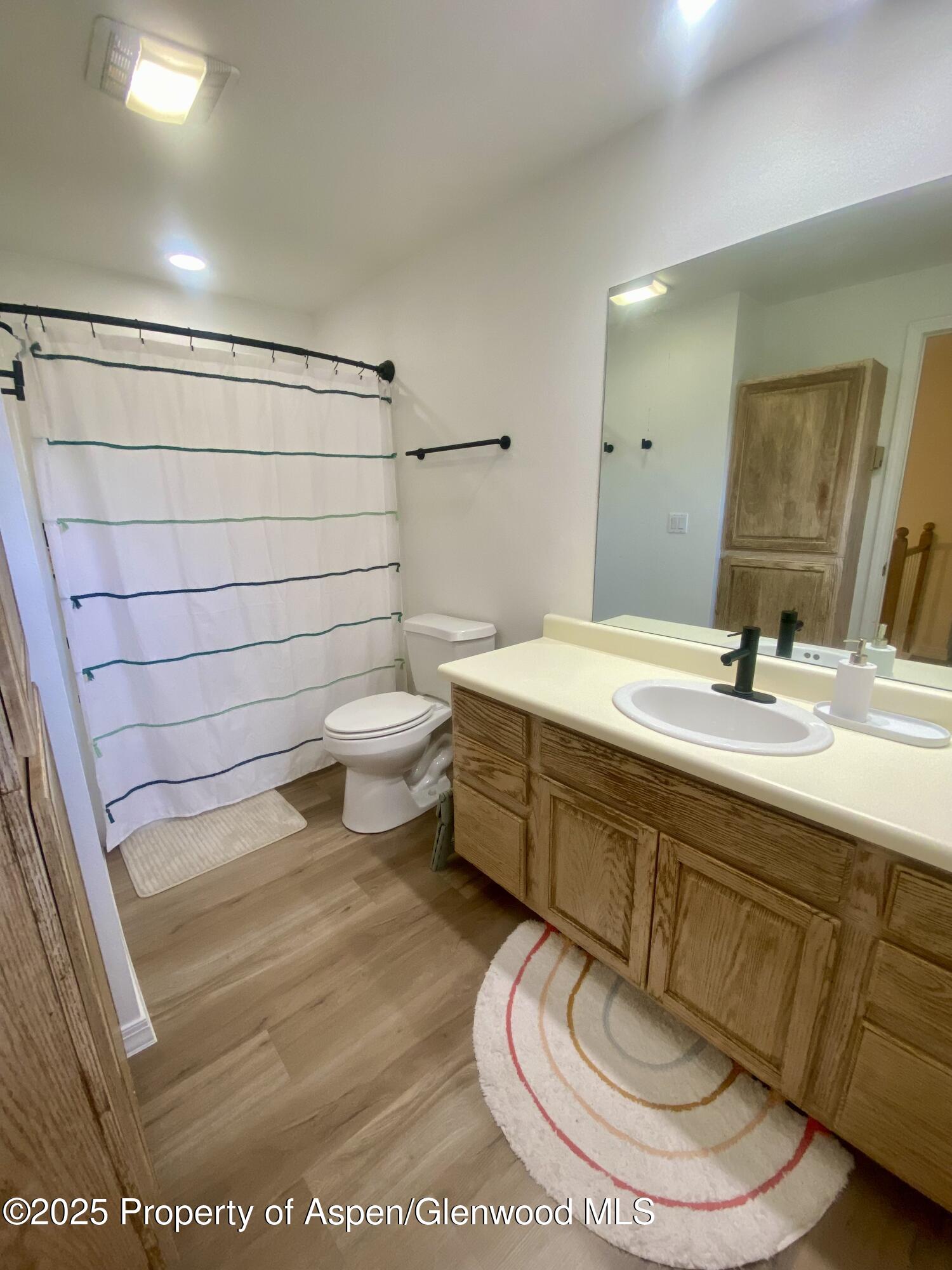 Bathroom with wood vanity, black faucet, large mirror, and striped shower curtain.