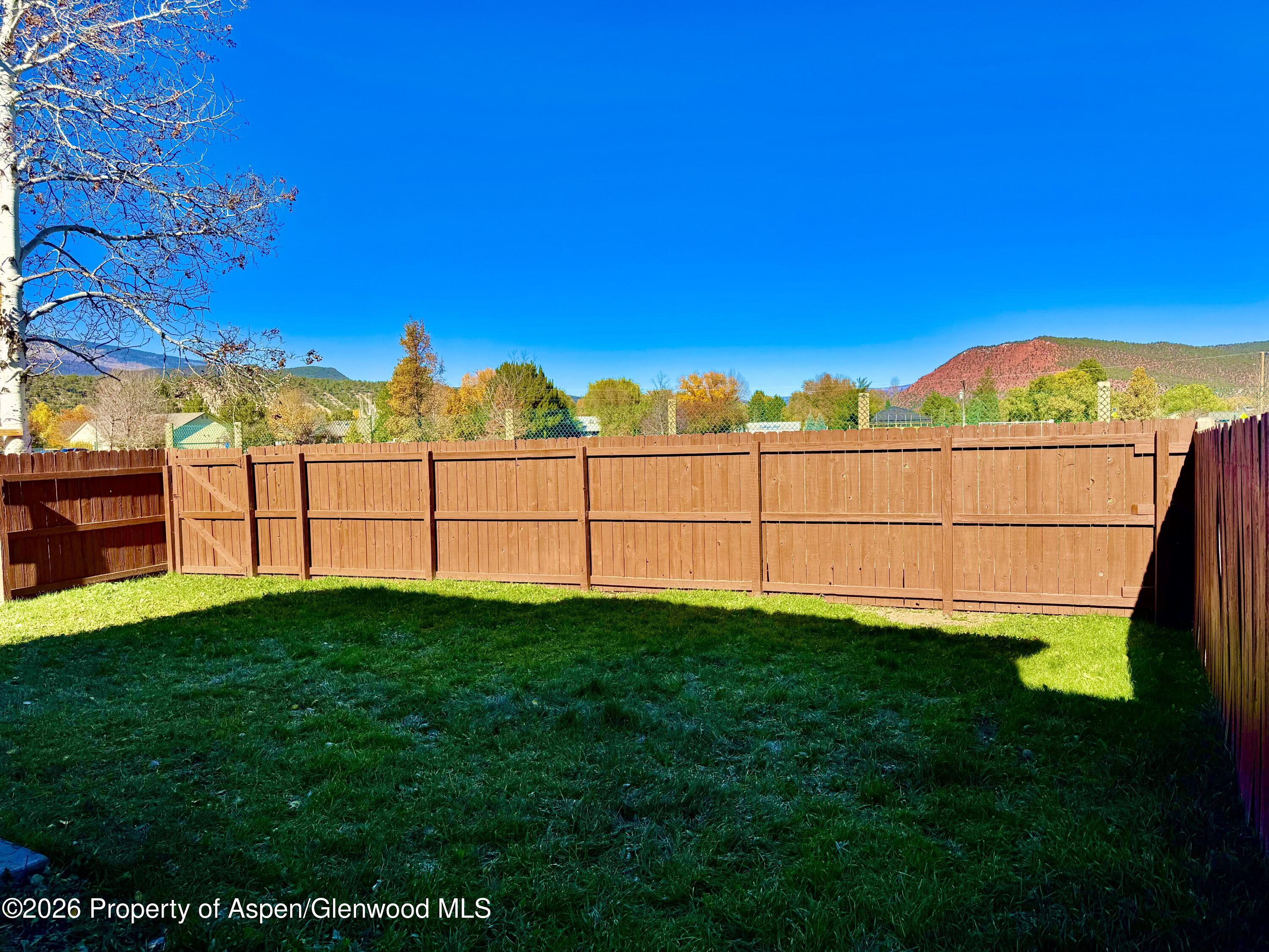 Fenced grassy backyard with a wooden gate and red rocky mountain in the distance.