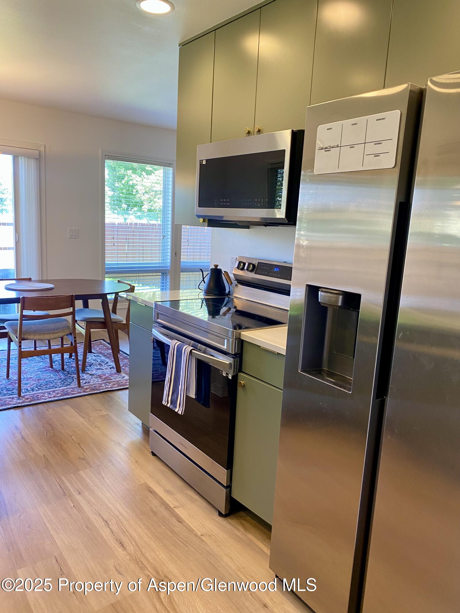 Kitchen with stainless steel appliances, muted green cabinets, and a dining table beside the windows.