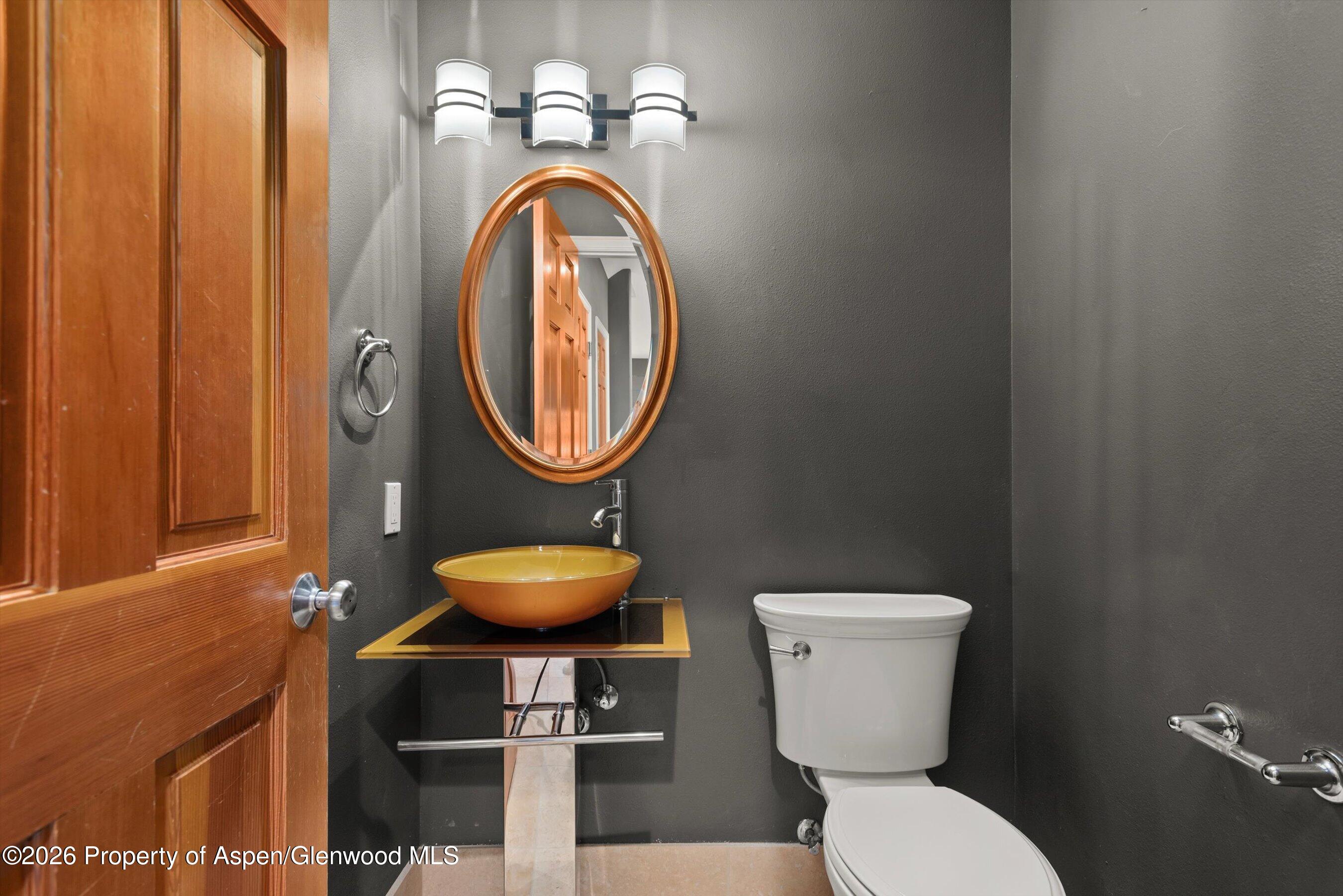 Bathroom with charcoal walls, a golden-orange vessel sink, oval mirror, and white toilet.