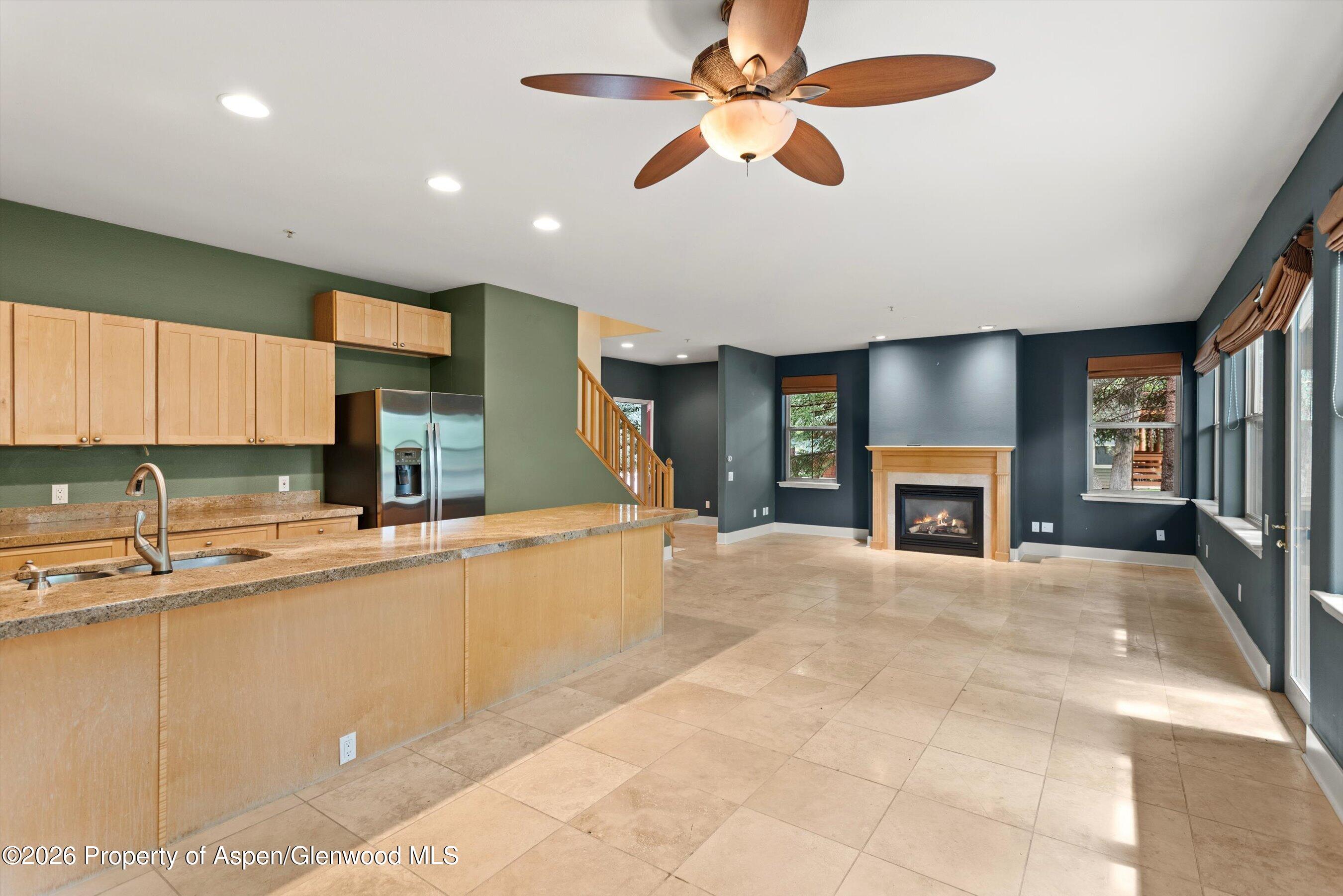 Open kitchen and living area with a granite island, tiled floors, and fireplace.