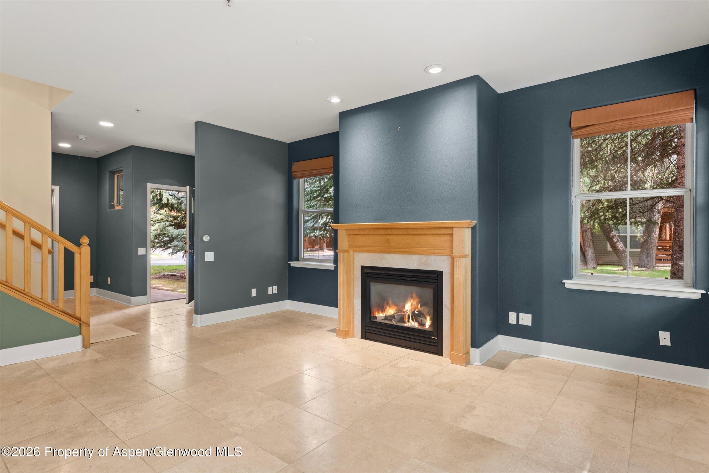 Unfurnished living room with a wood-trimmed fireplace, large windows, and beige tile flooring.
