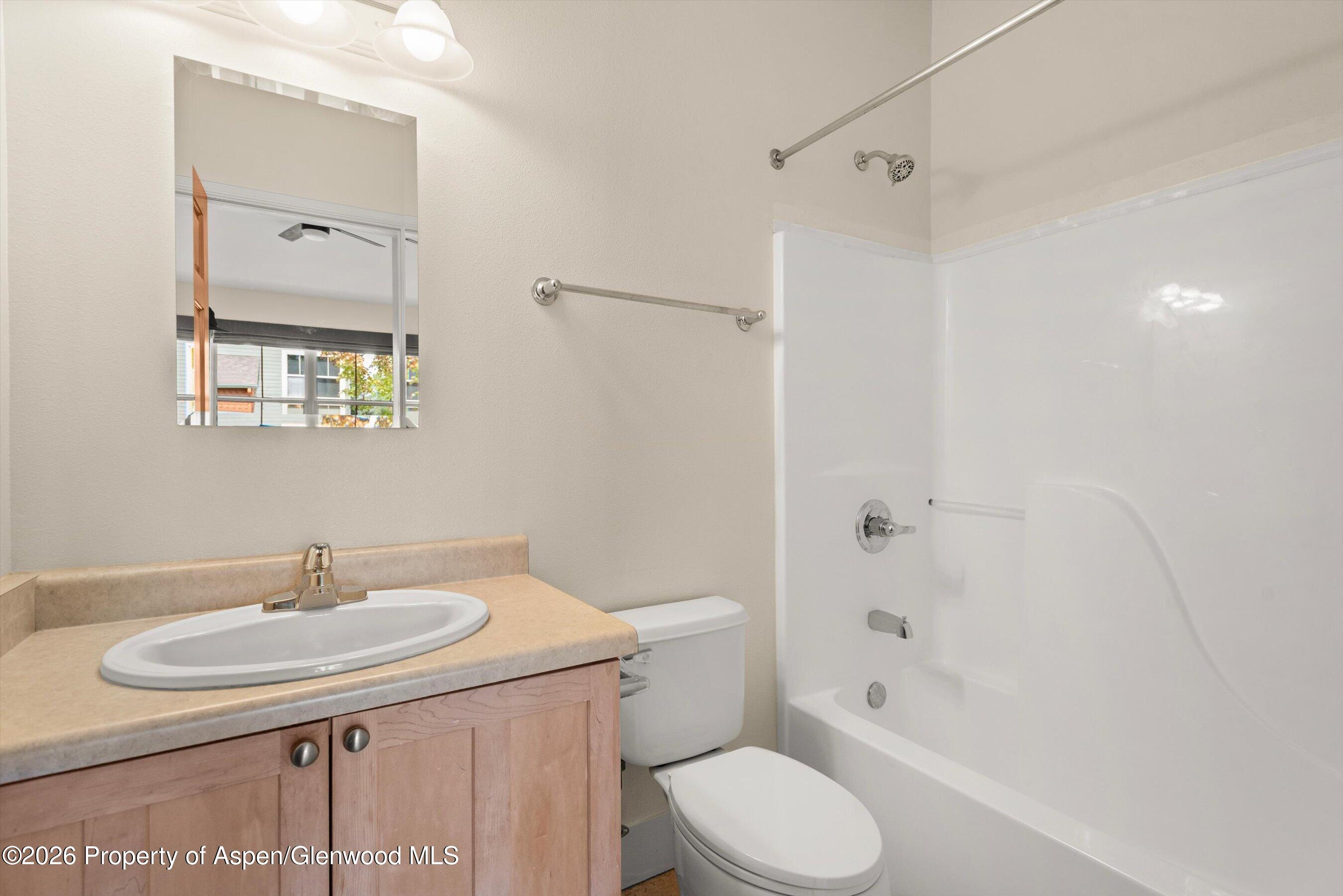 Bathroom with a wood vanity, oval sink, toilet, and white tub-shower.
