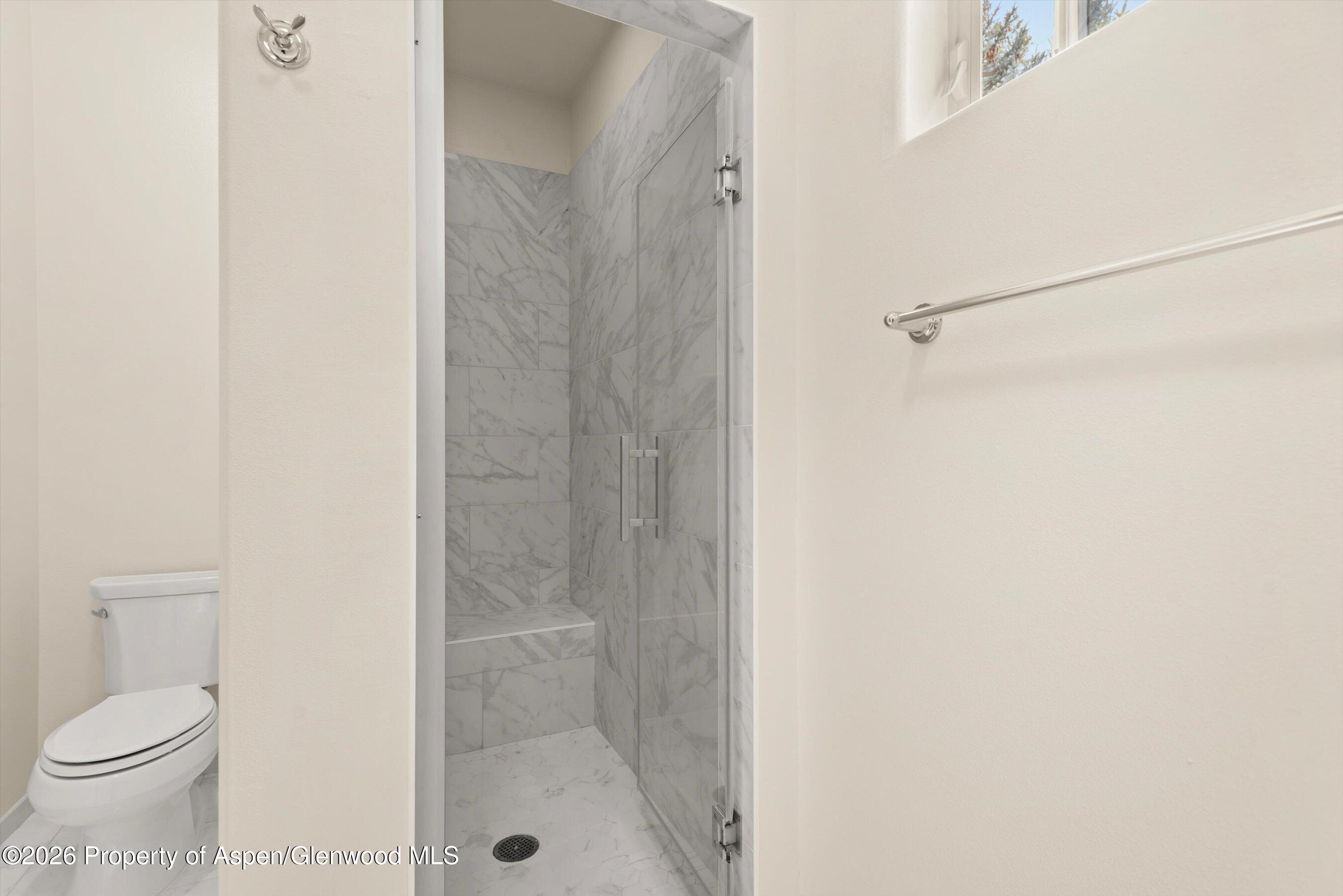 Bathroom with a marble-tiled walk-in shower, built-in bench, and adjacent toilet.