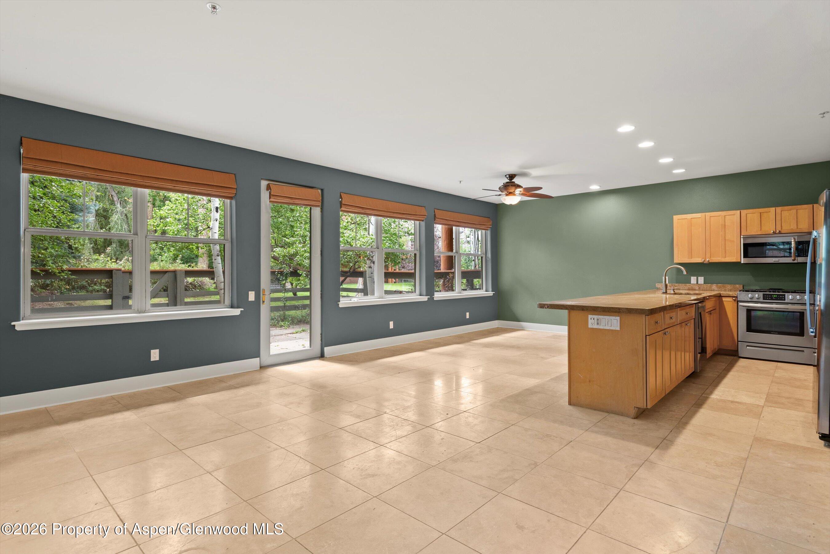 Vacant kitchen with a large wood island, tiled floors, and windows overlooking leafy greenery.