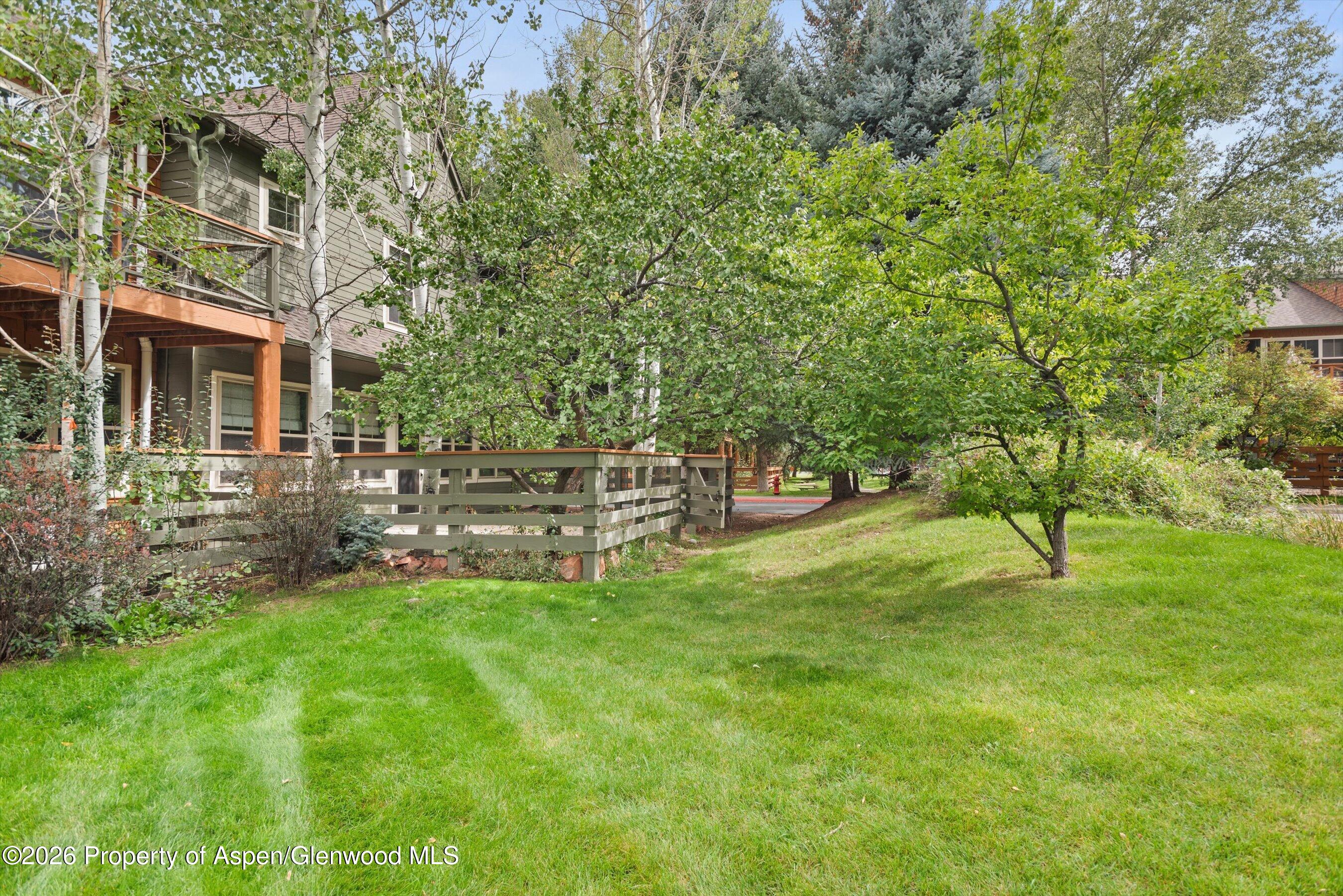 House exterior with a raised wooden deck behind leafy trees and a broad green lawn.