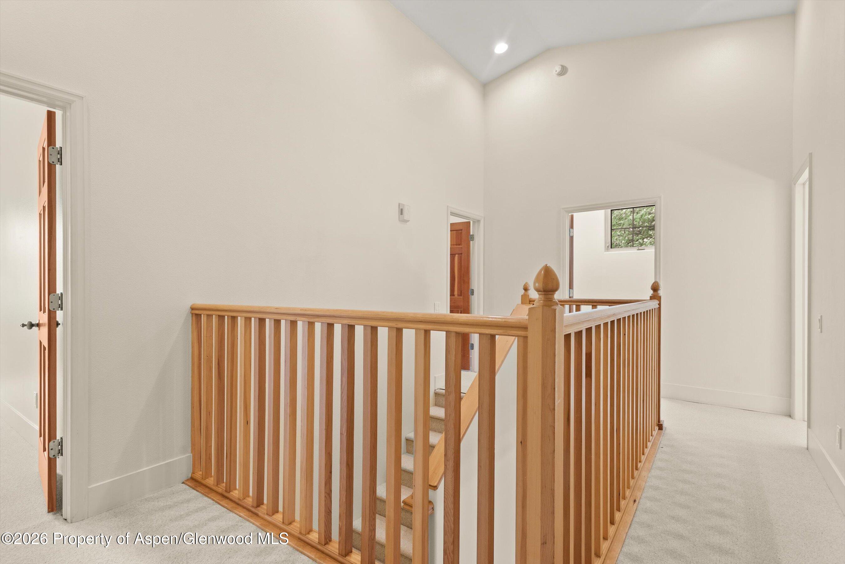 Upstairs landing with a honey-toned wood stair railing, carpeted floor, and open doorways.