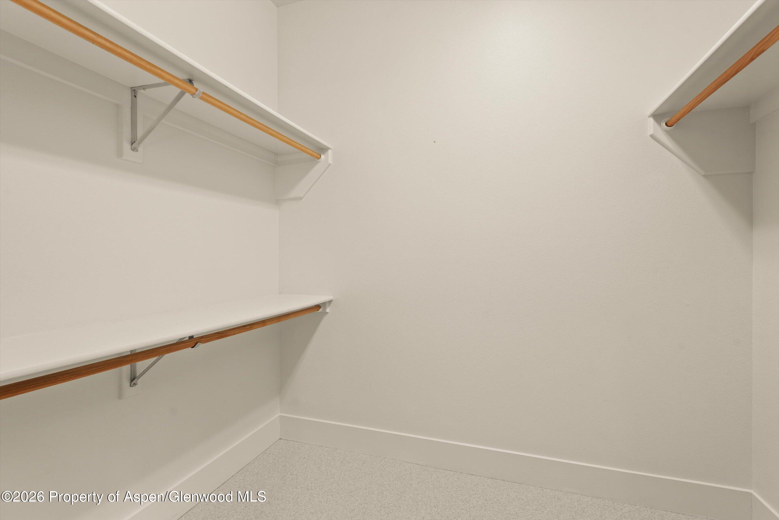 Empty walk-in closet with white shelving, wooden hanging rods, and light carpet.