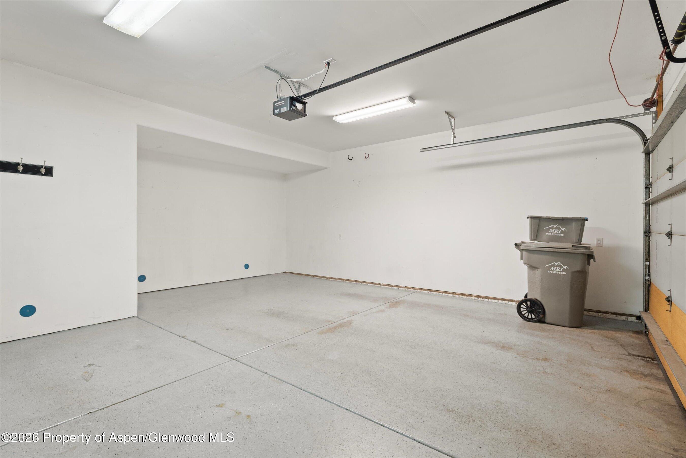 Vacant garage with a concrete floor, overhead door tracks, and two wheeled bins.