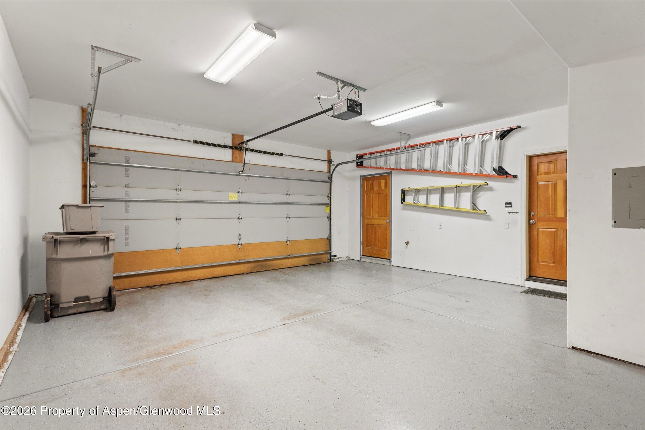 Garage with a large overhead door, wall-mounted ladders, and two wooden entry doors.