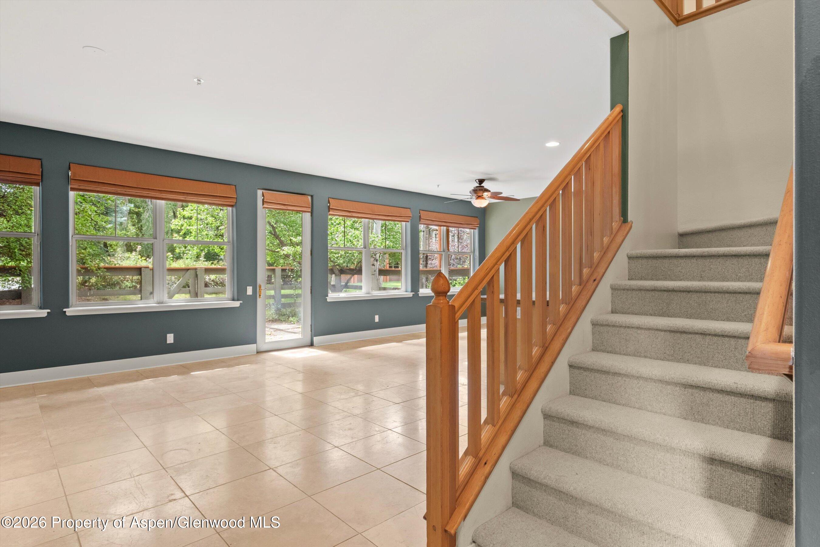 Empty tiled room with large windows beside a carpeted staircase with a wooden railing.