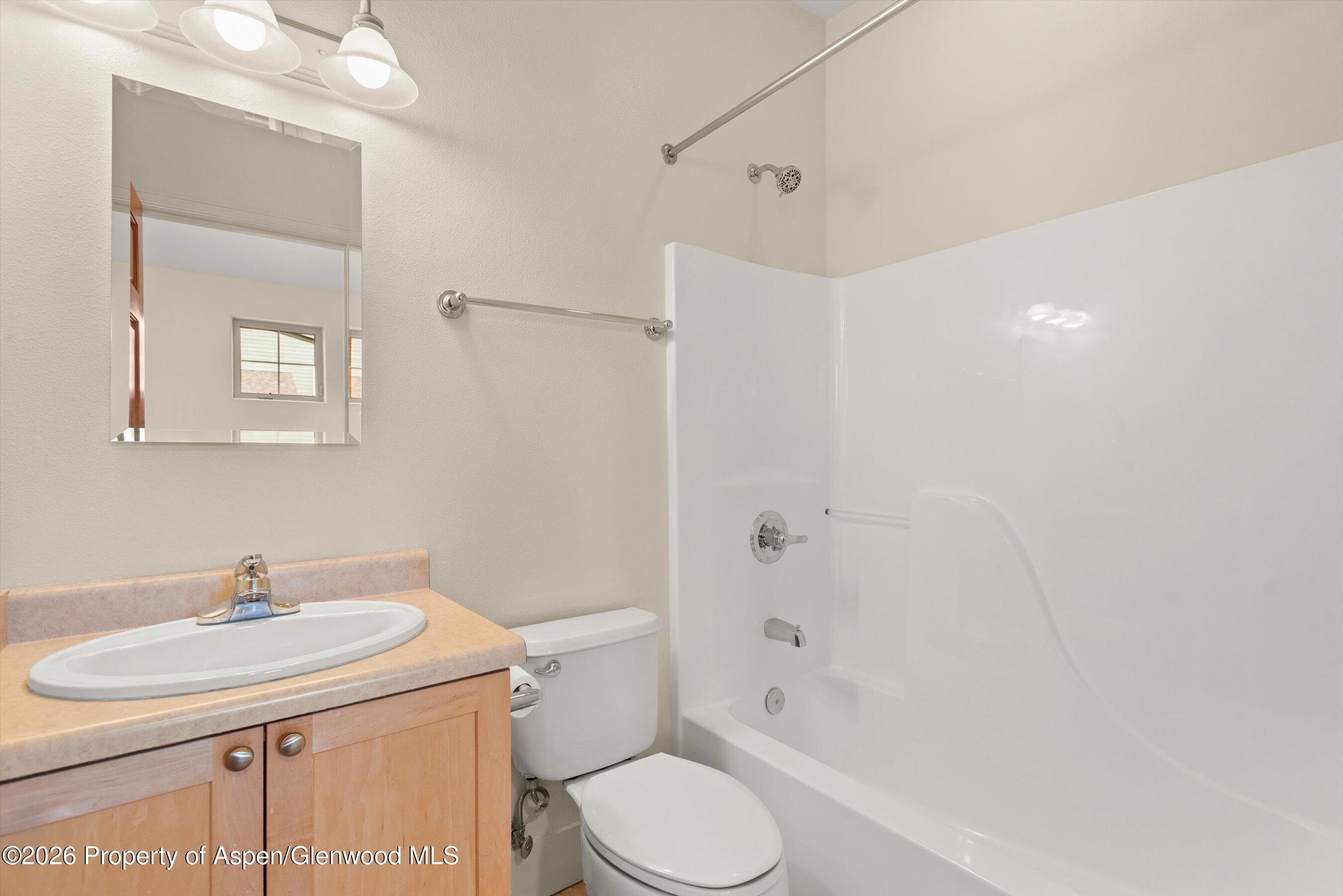 Bathroom with a white tub and shower beside a light wood vanity and oval sink.