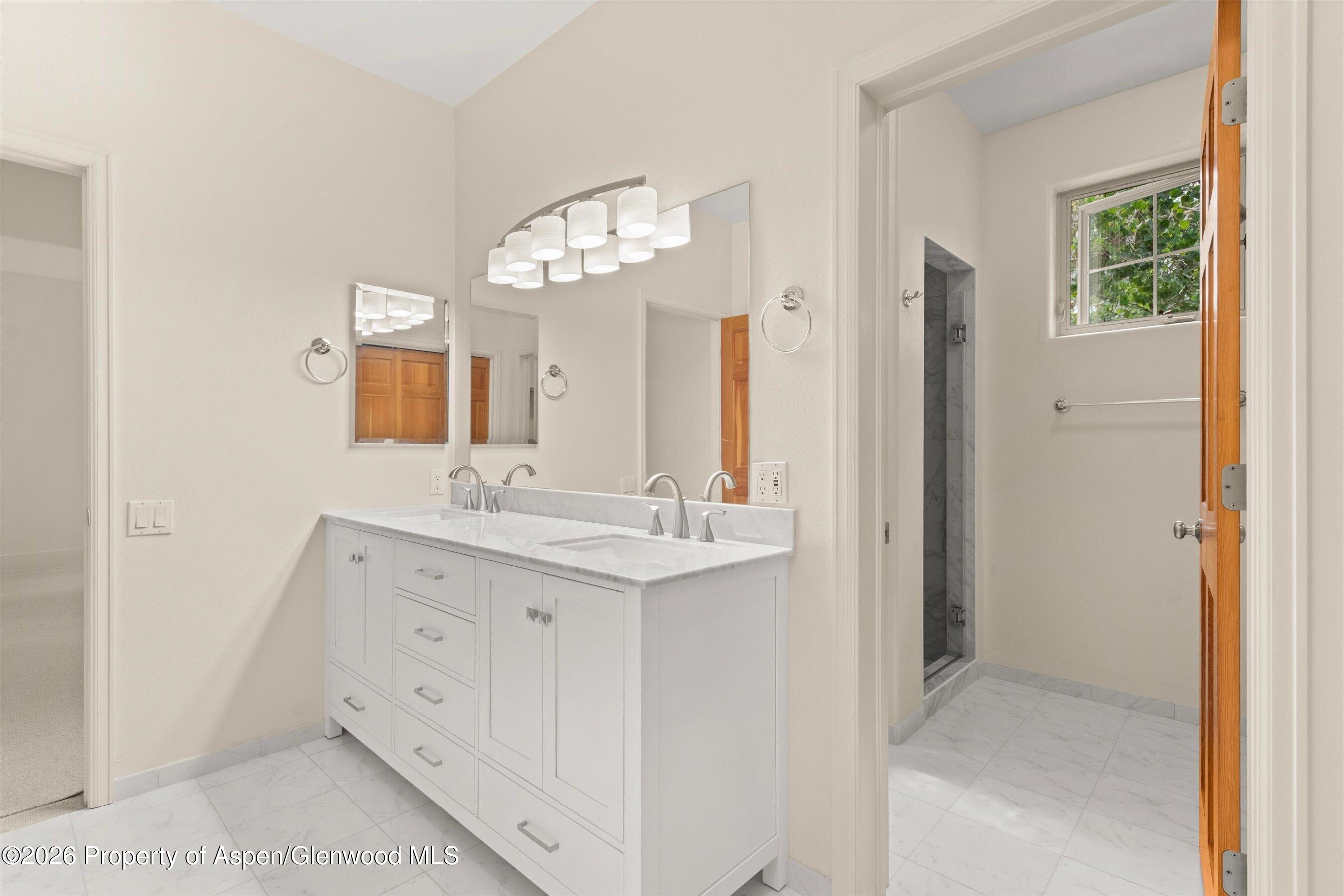 Bright bathroom with a long double-sink vanity, large mirrors, and an adjoining walk-in shower.
