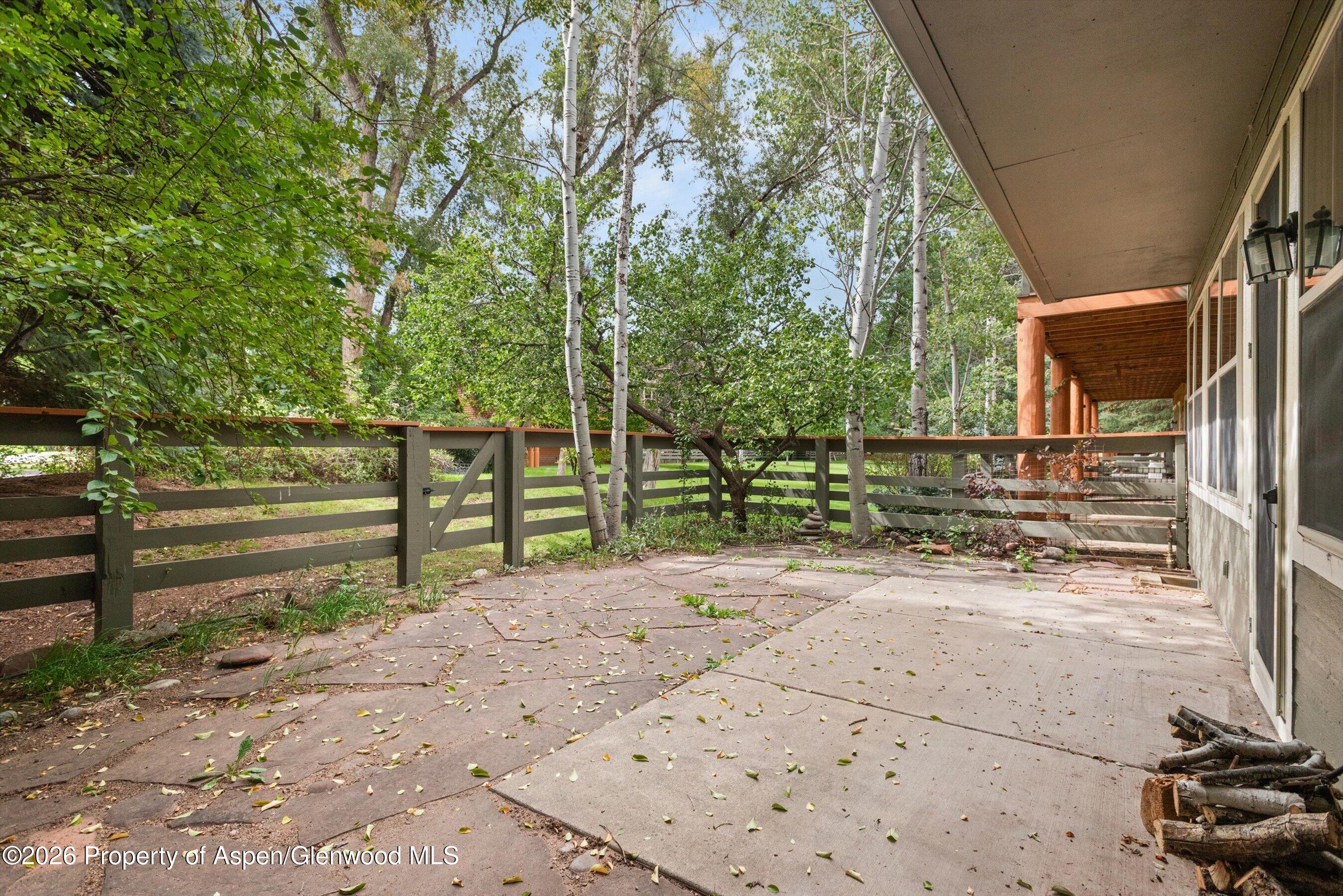 Stone patio beside a covered porch, enclosed by a wood fence and leafy aspens.