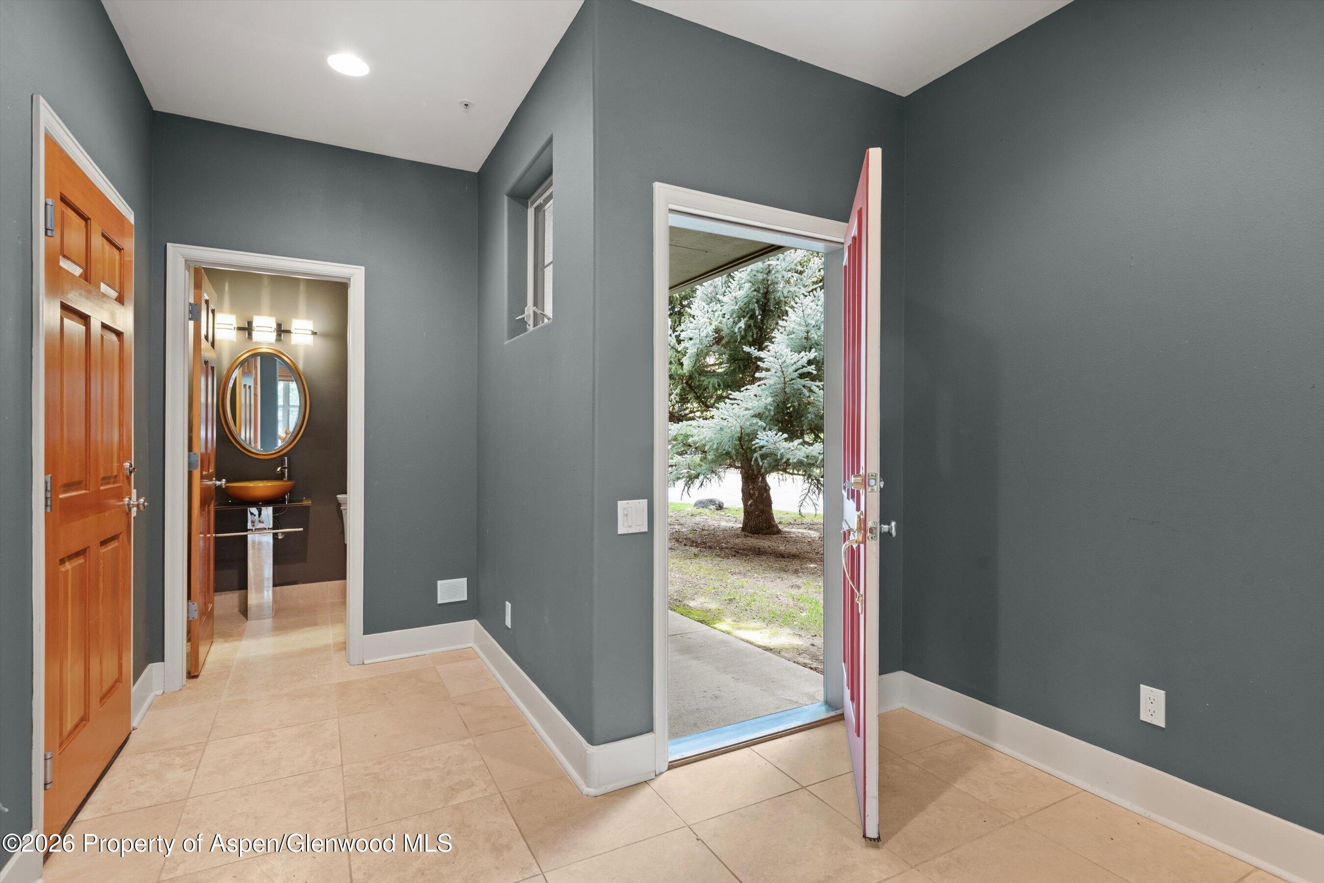 Entry foyer with beige tile floors and an open red door beside a powder room.