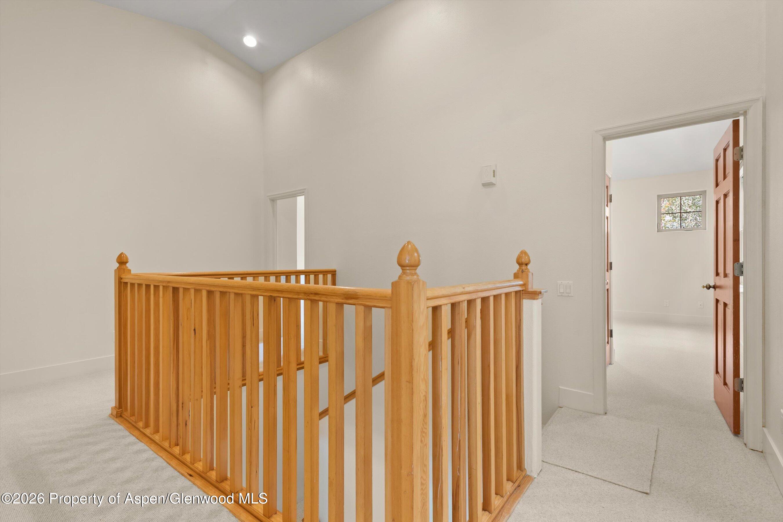 Carpeted upstairs landing with a wooden stair railing and an open door to a bright room.