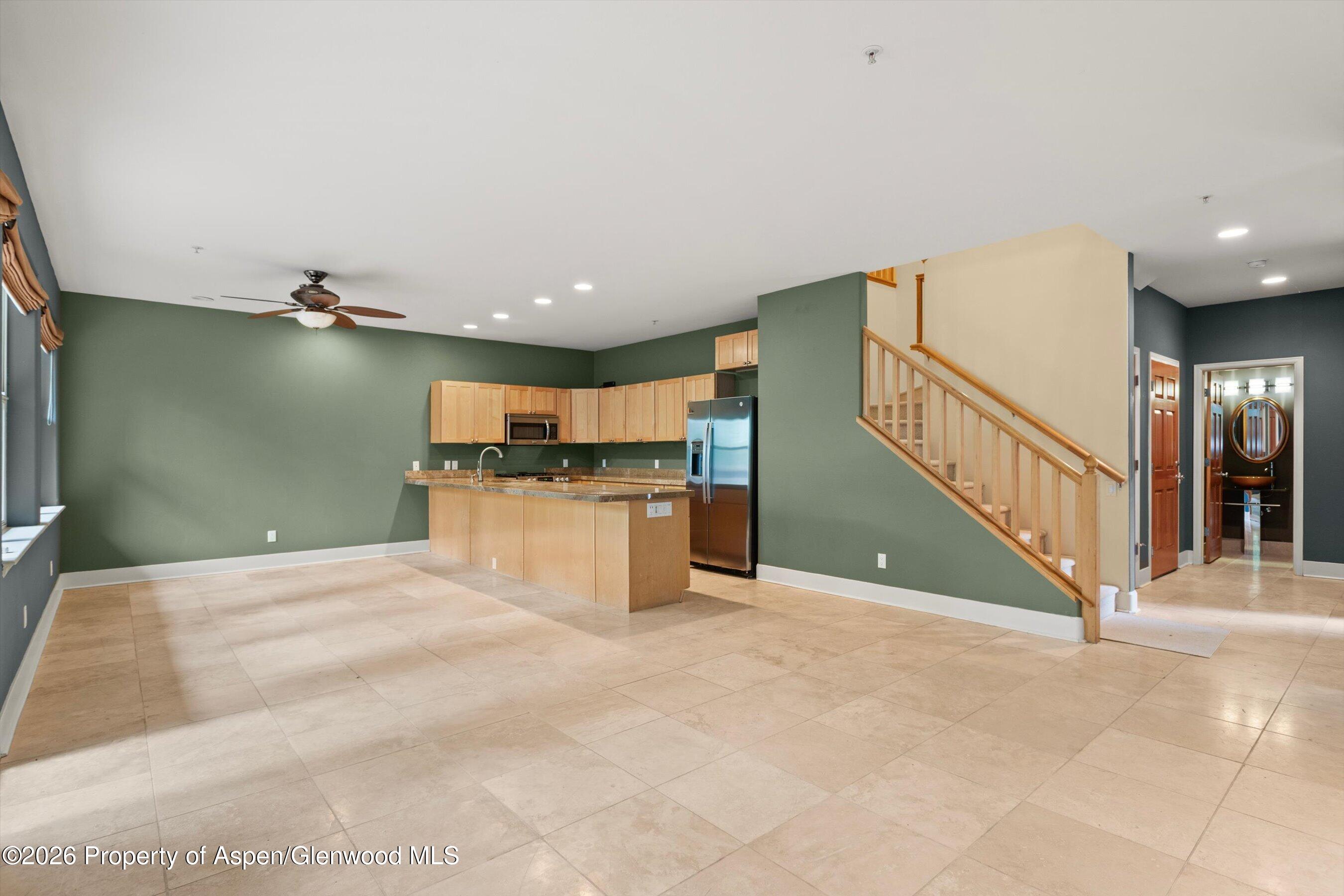 Open-plan kitchen and living area with a granite island, light wood cabinets, and staircase.