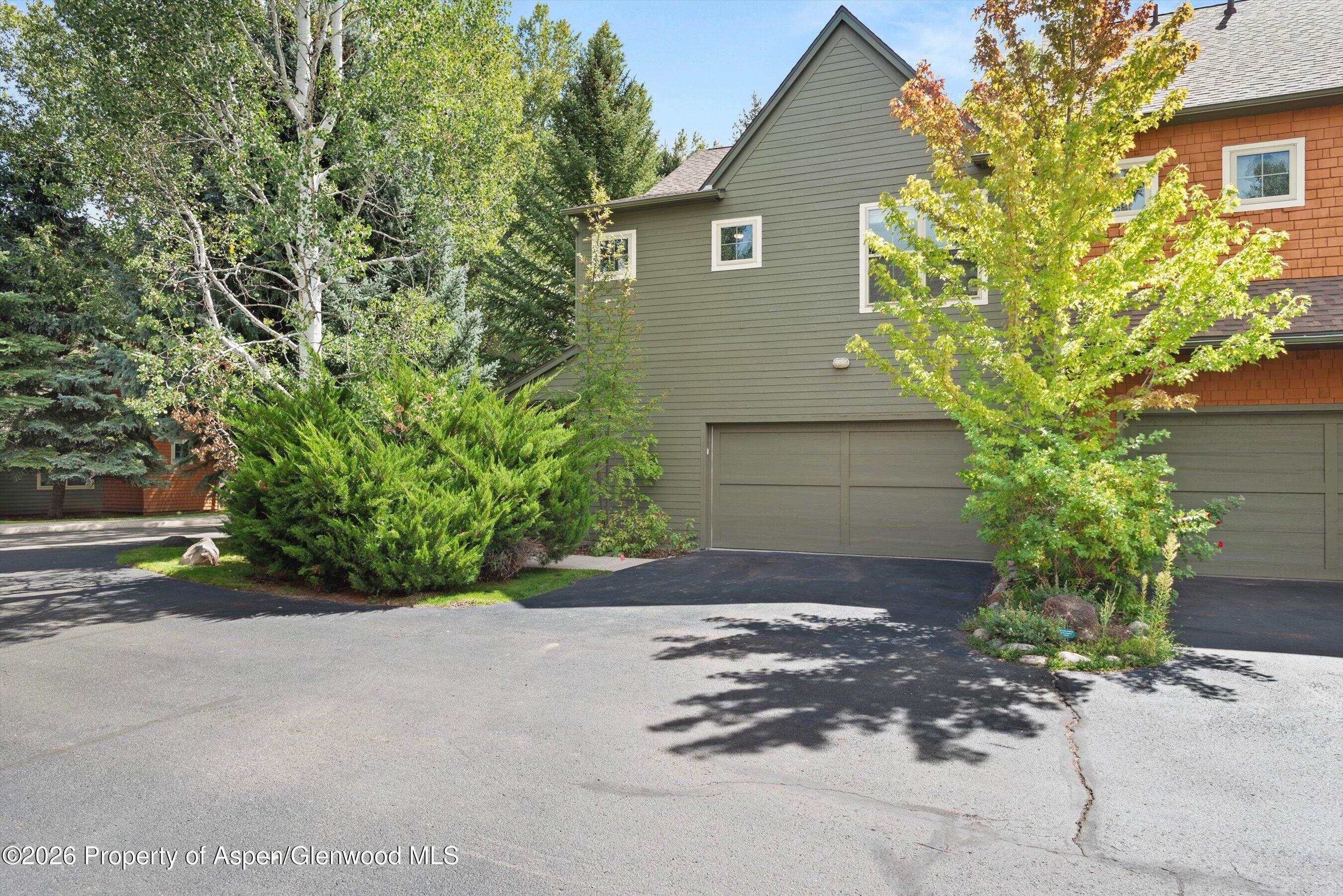 Home exterior with green siding, orange shingle accents, double garage, and mature landscaping.