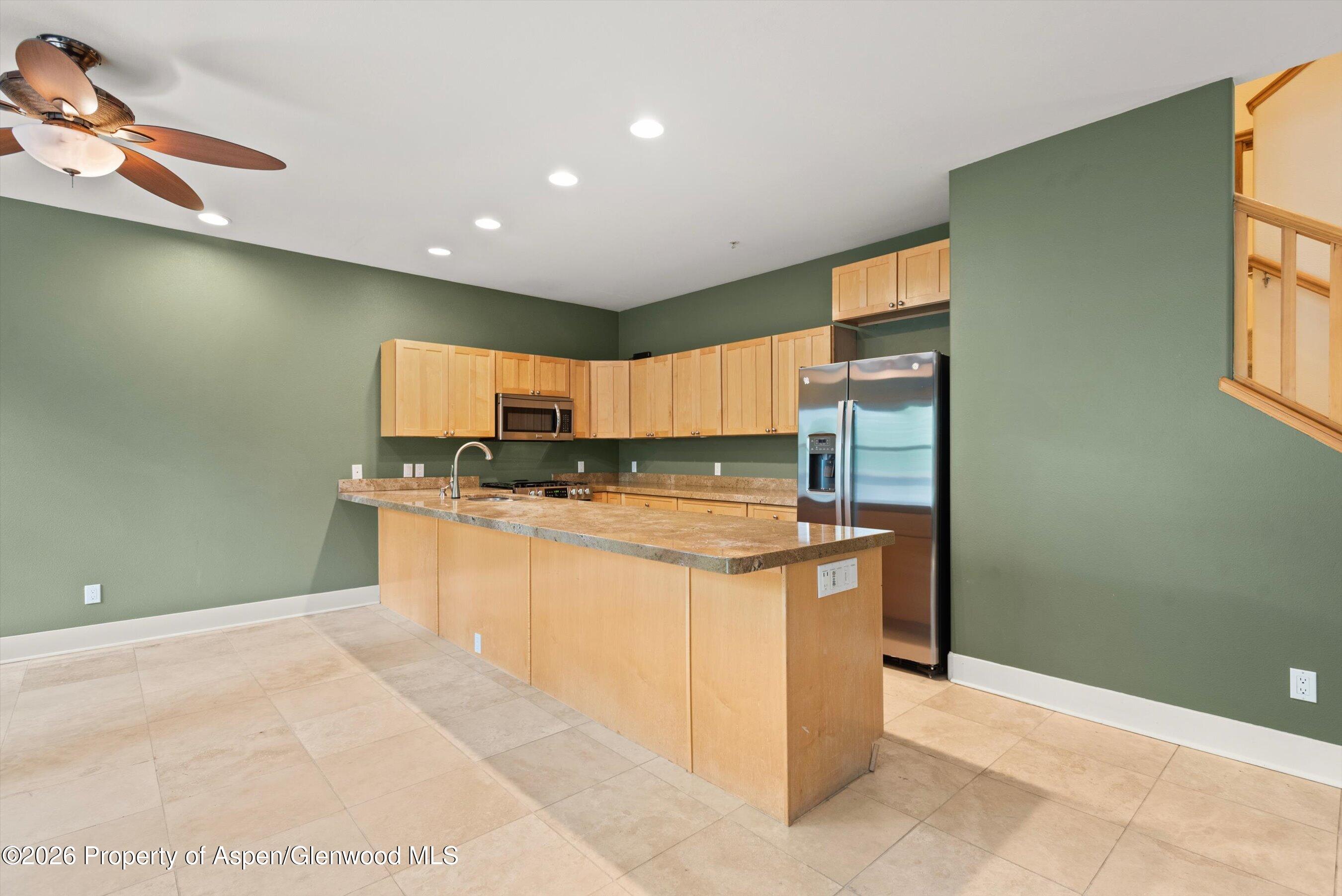 Kitchen with a large stone-topped island, light wood cabinets, and stainless steel appliances.