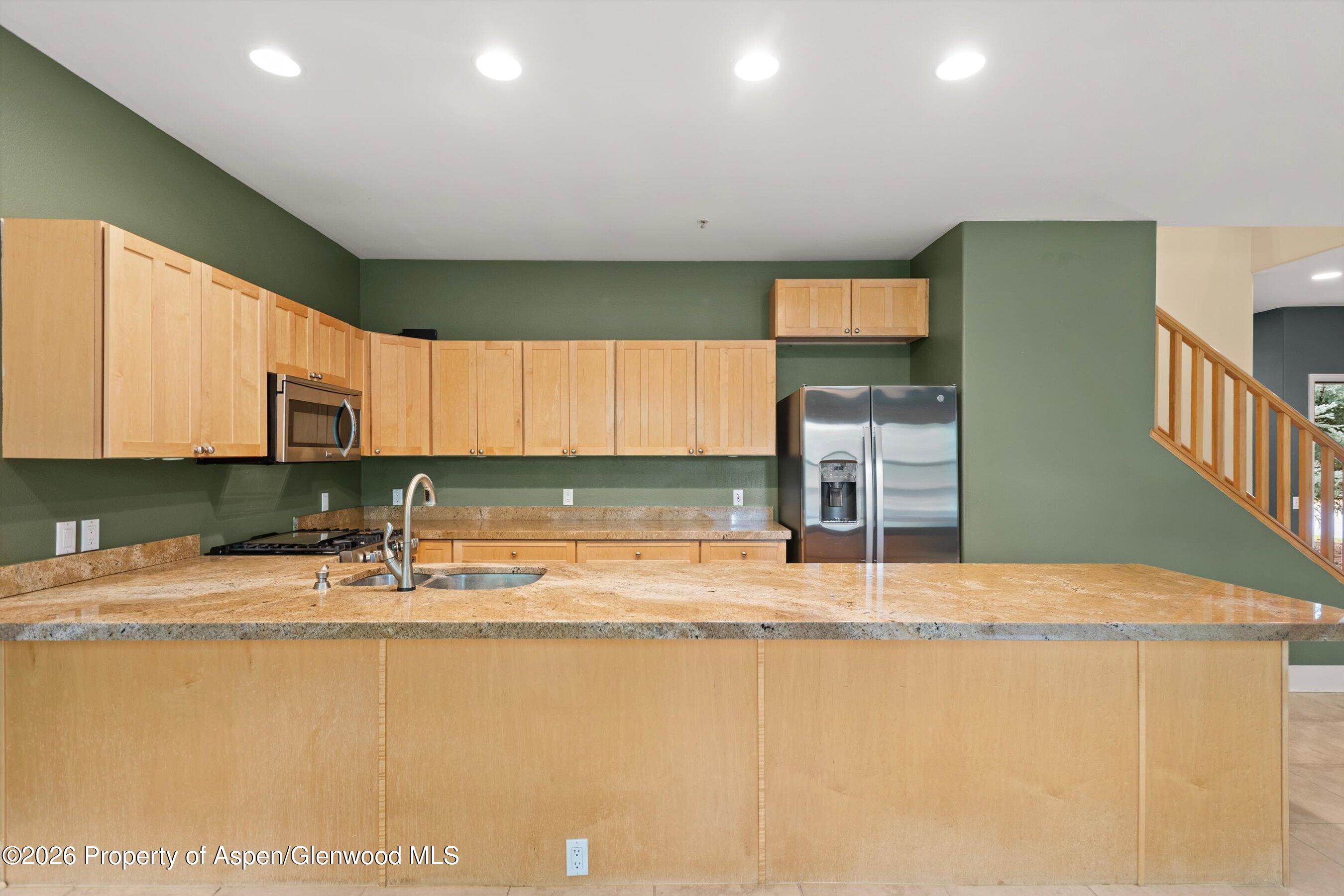 Kitchen with light wood cabinets, green walls, stainless appliances, and a large stone island.
