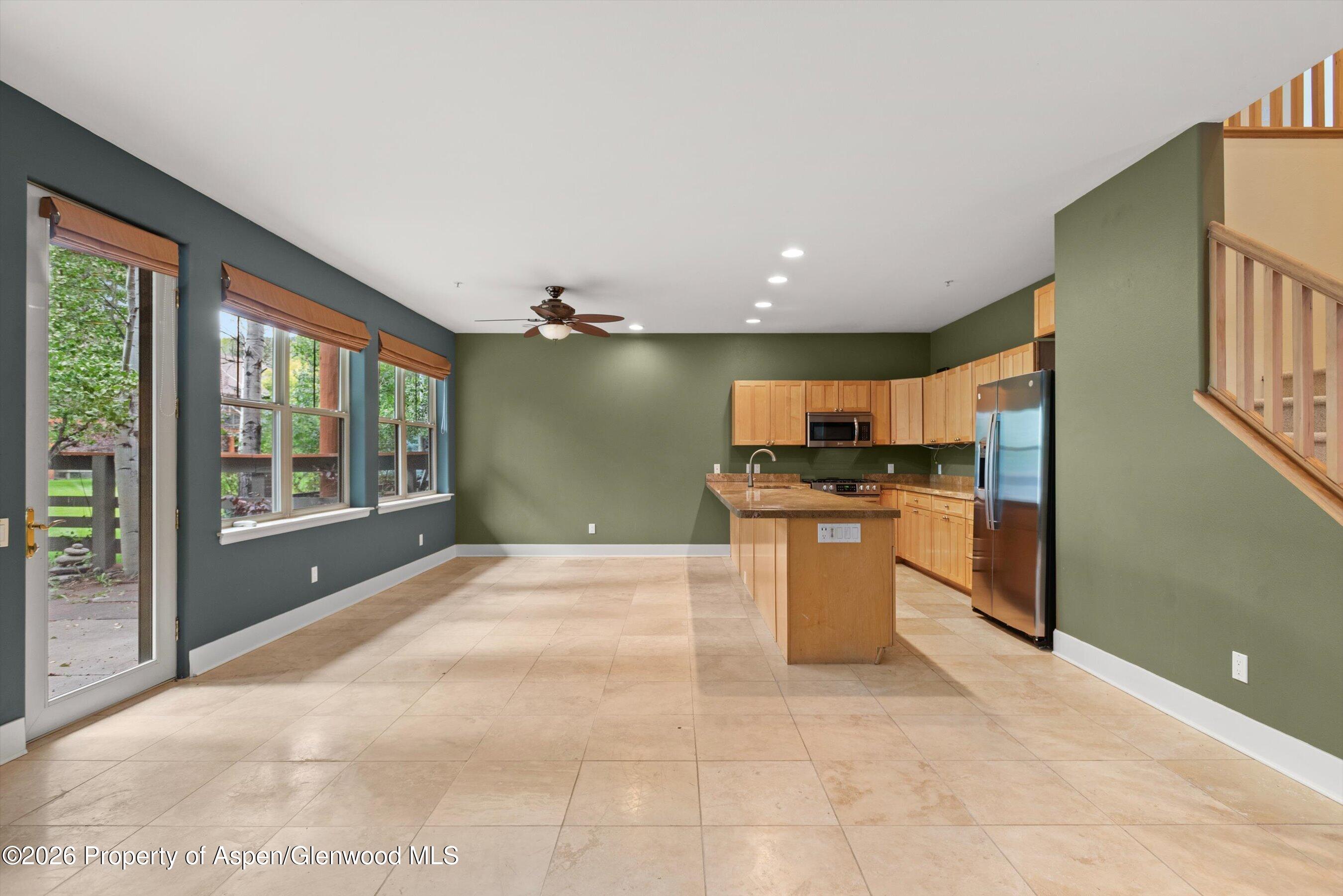 Unfurnished kitchen with a stone-topped island, light wood cabinets, and large windows beside the dining area.