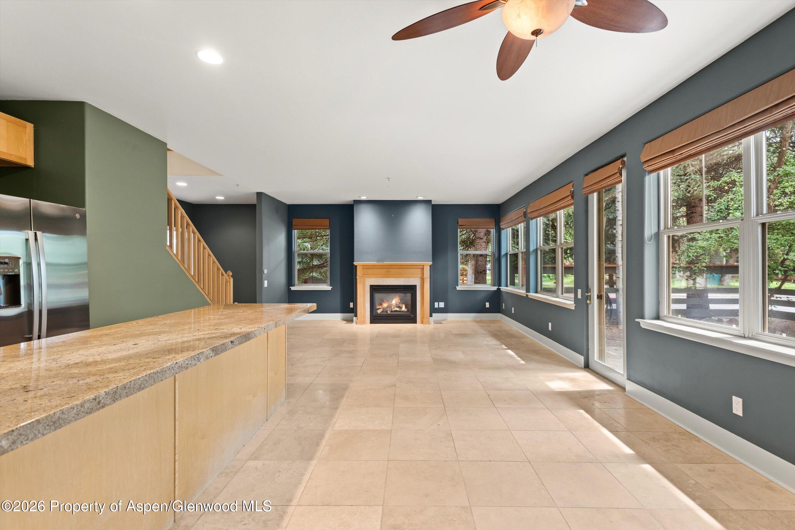 Open living area with a gas fireplace, granite kitchen island, and large windows overlooking trees.