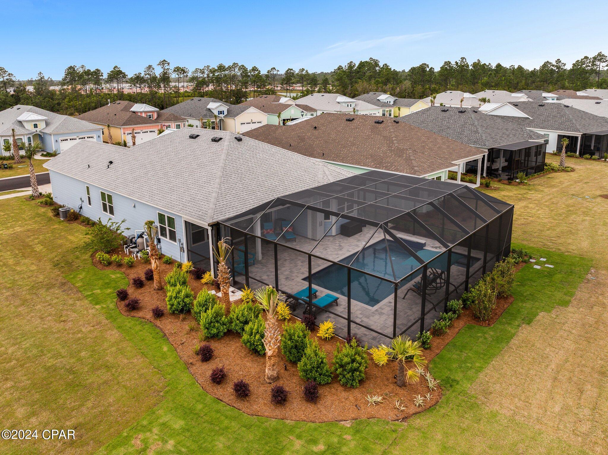 Aerial view of a home with a screened-in pool, paved patio, and landscaped garden.