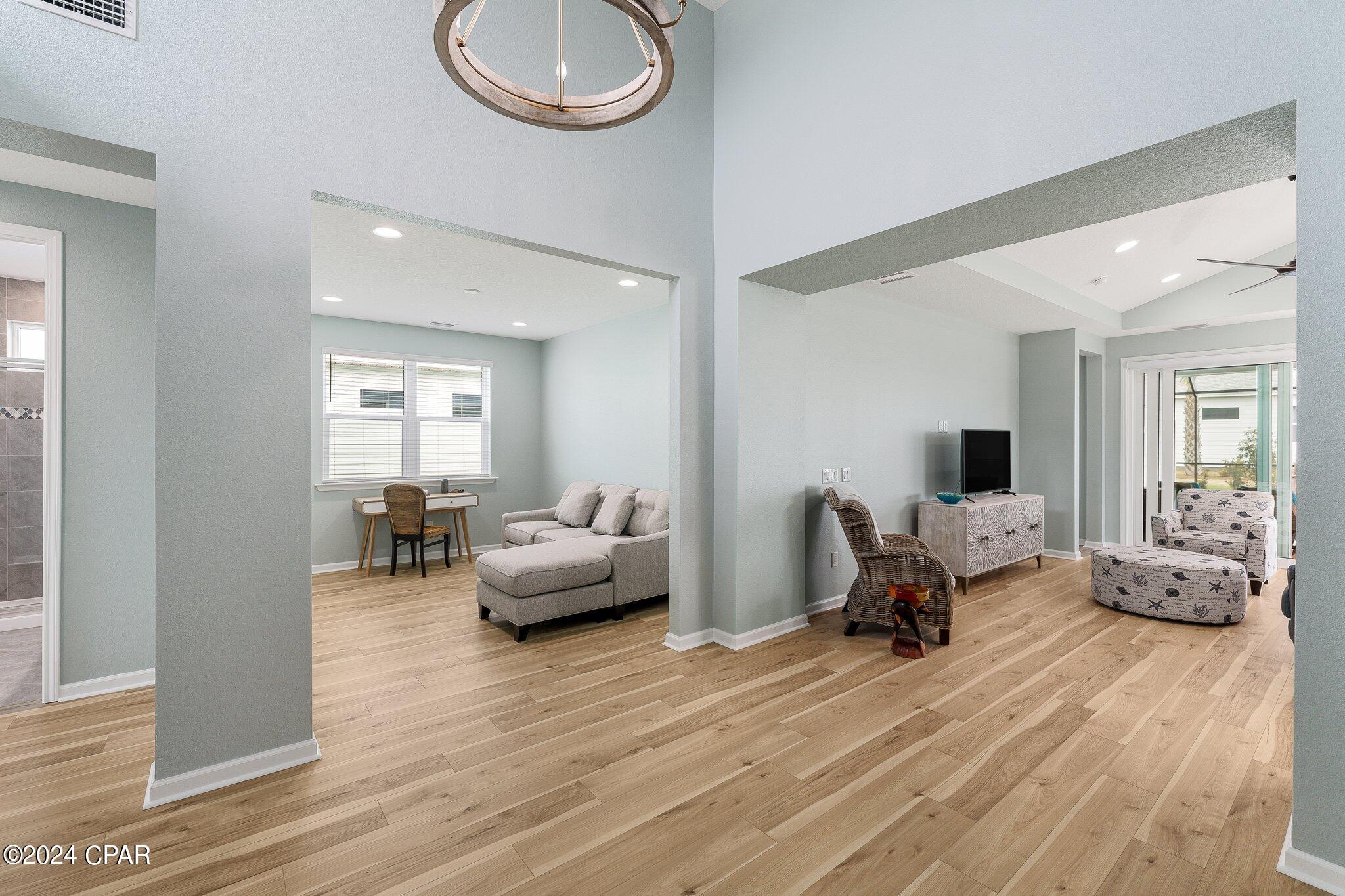 Open-plan living area with a gray sectional, adjoining desk nook, and light wood floors.