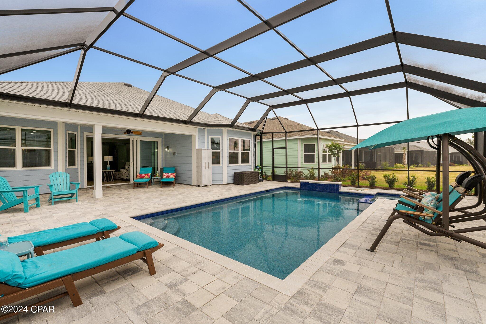 Screened backyard pool and patio with turquoise loungers and a covered swing.