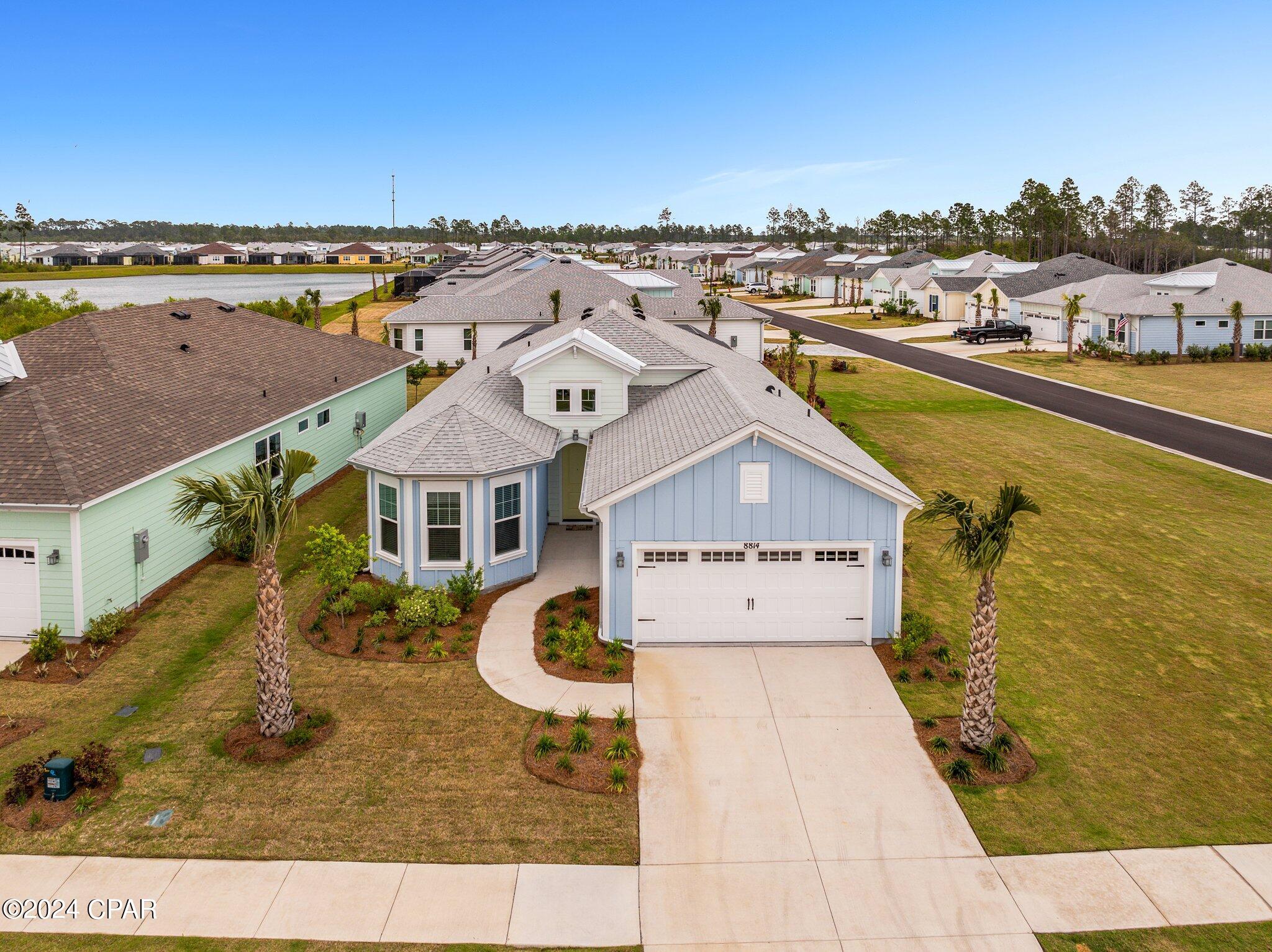 Aerial view of a pale blue house with a white roof, two-car garage, and palm trees.