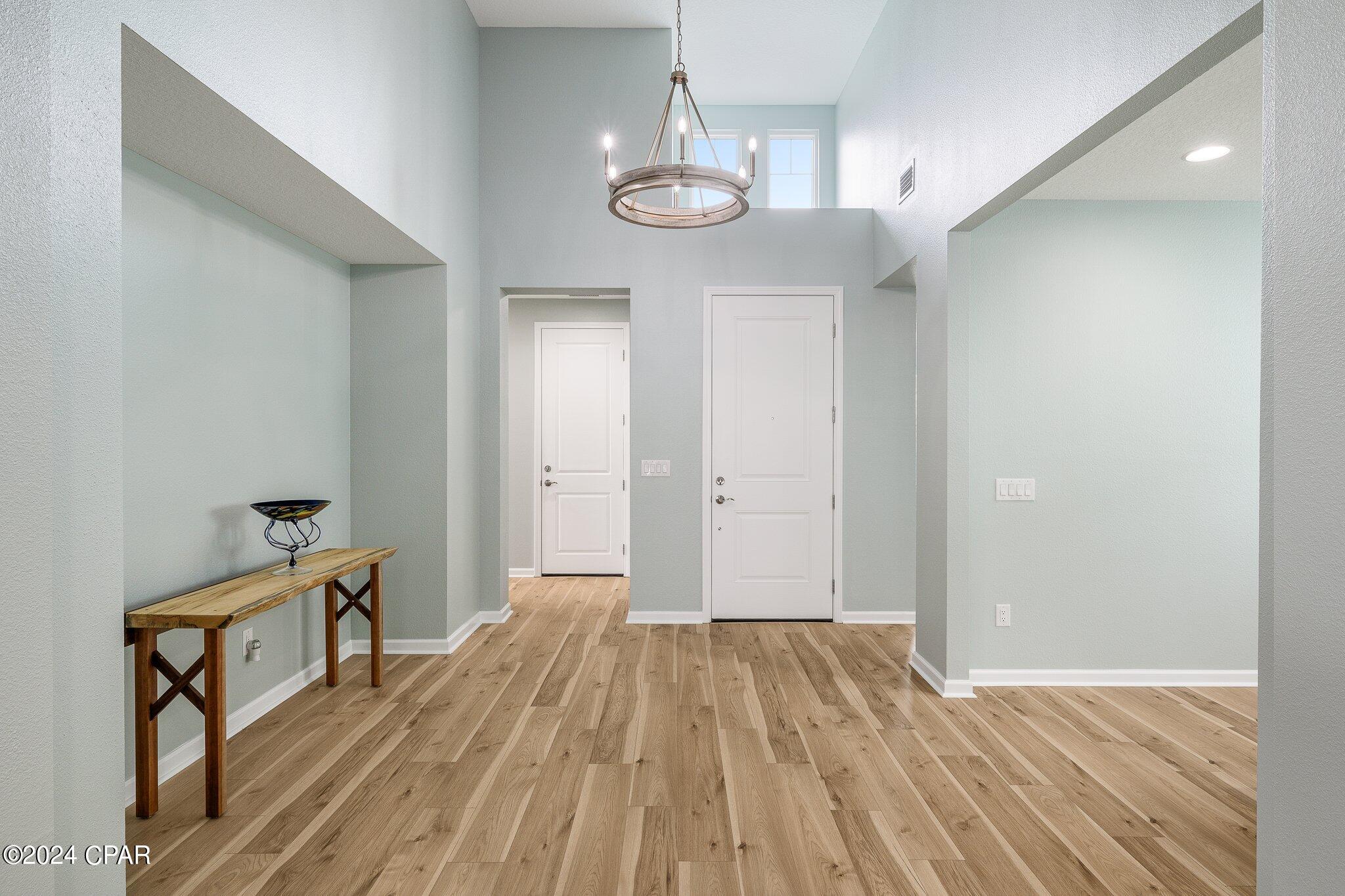Entry foyer with a high ceiling, circular chandelier, light wood floors, and a narrow console table.
