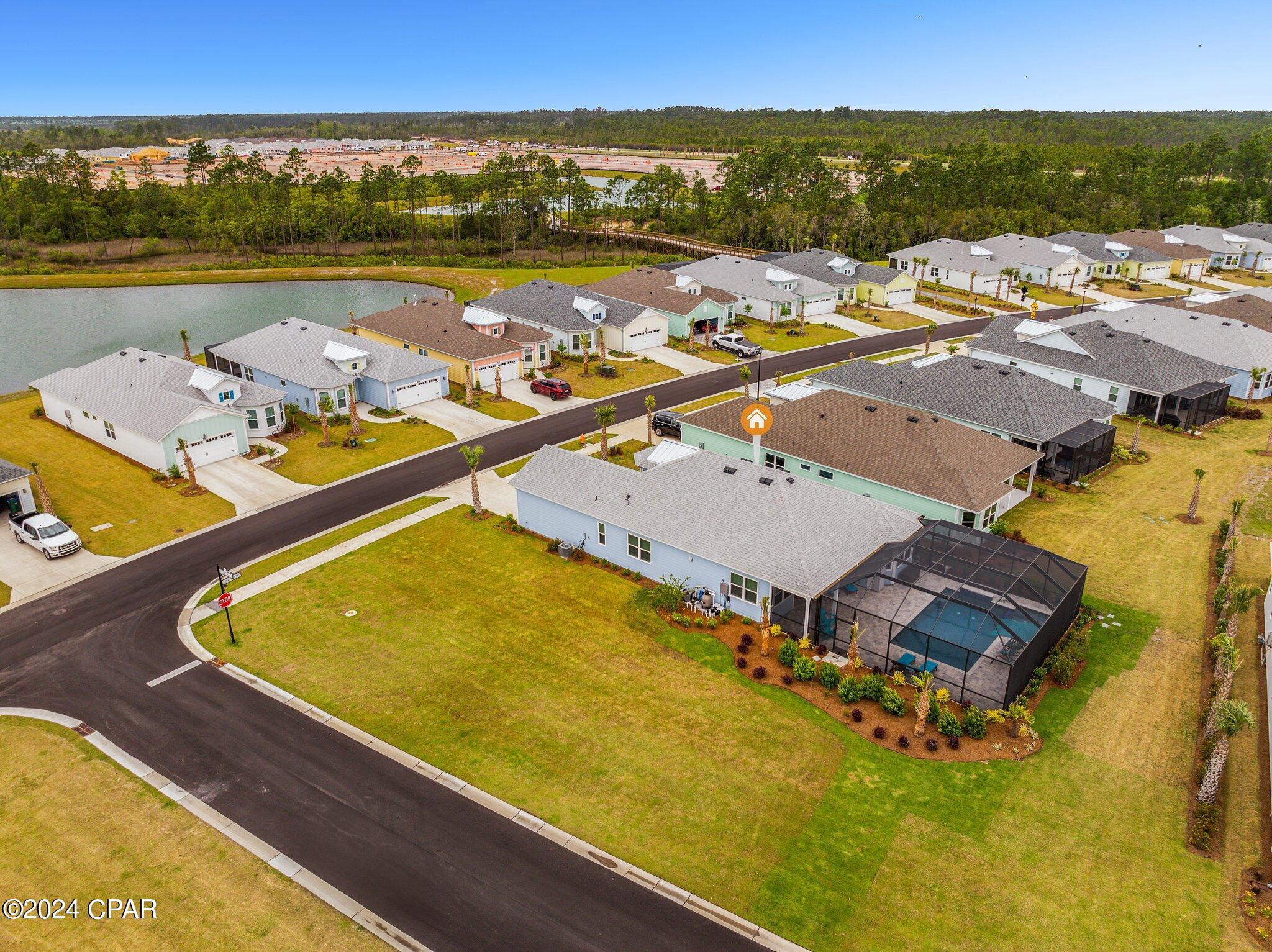 Aerial view of a light-blue home with a large screened lanai, marked among neighboring homes beside a pond.