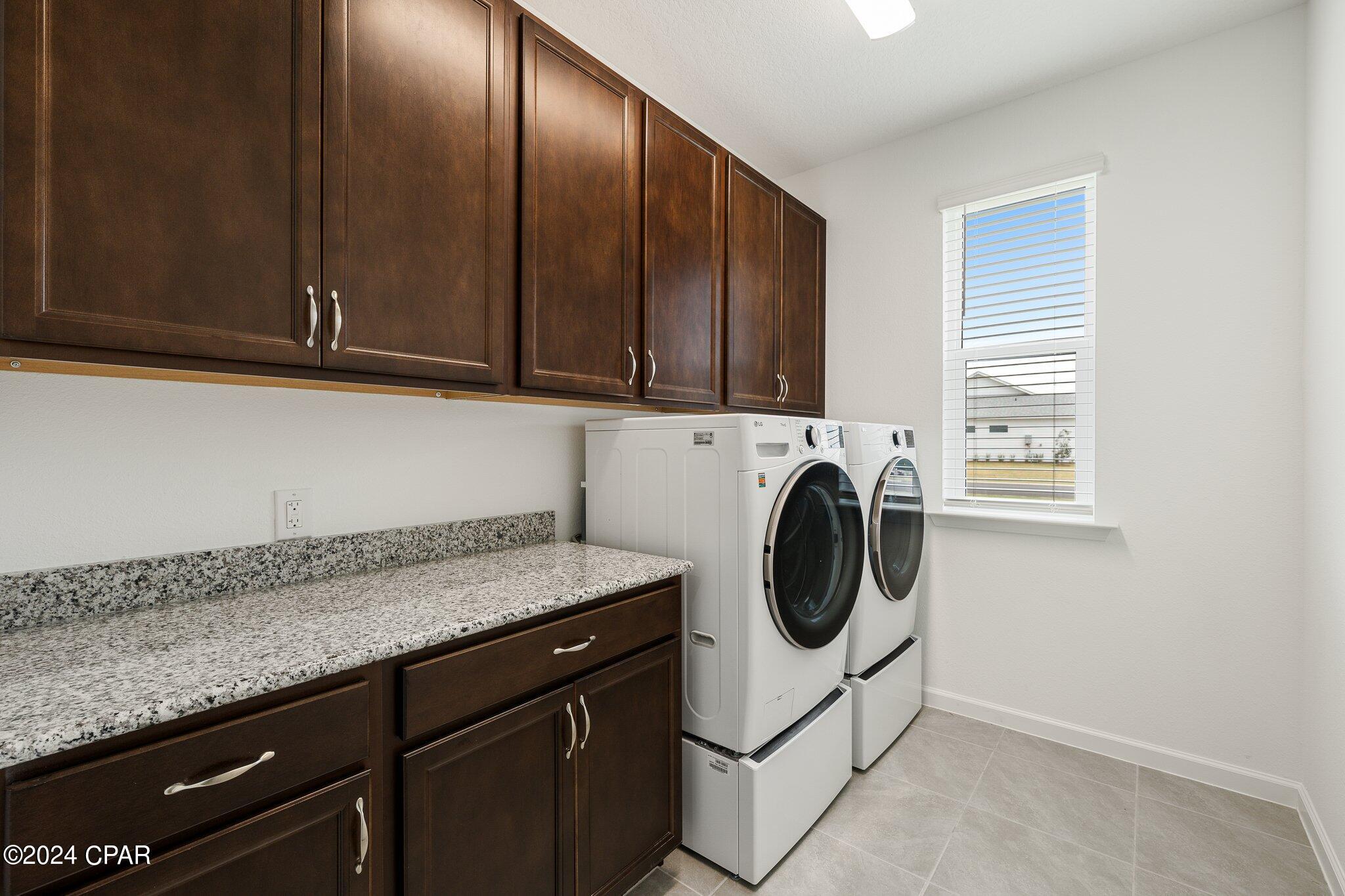 Laundry room with dark wood cabinets, granite counter, and white front-loading washer and dryer.