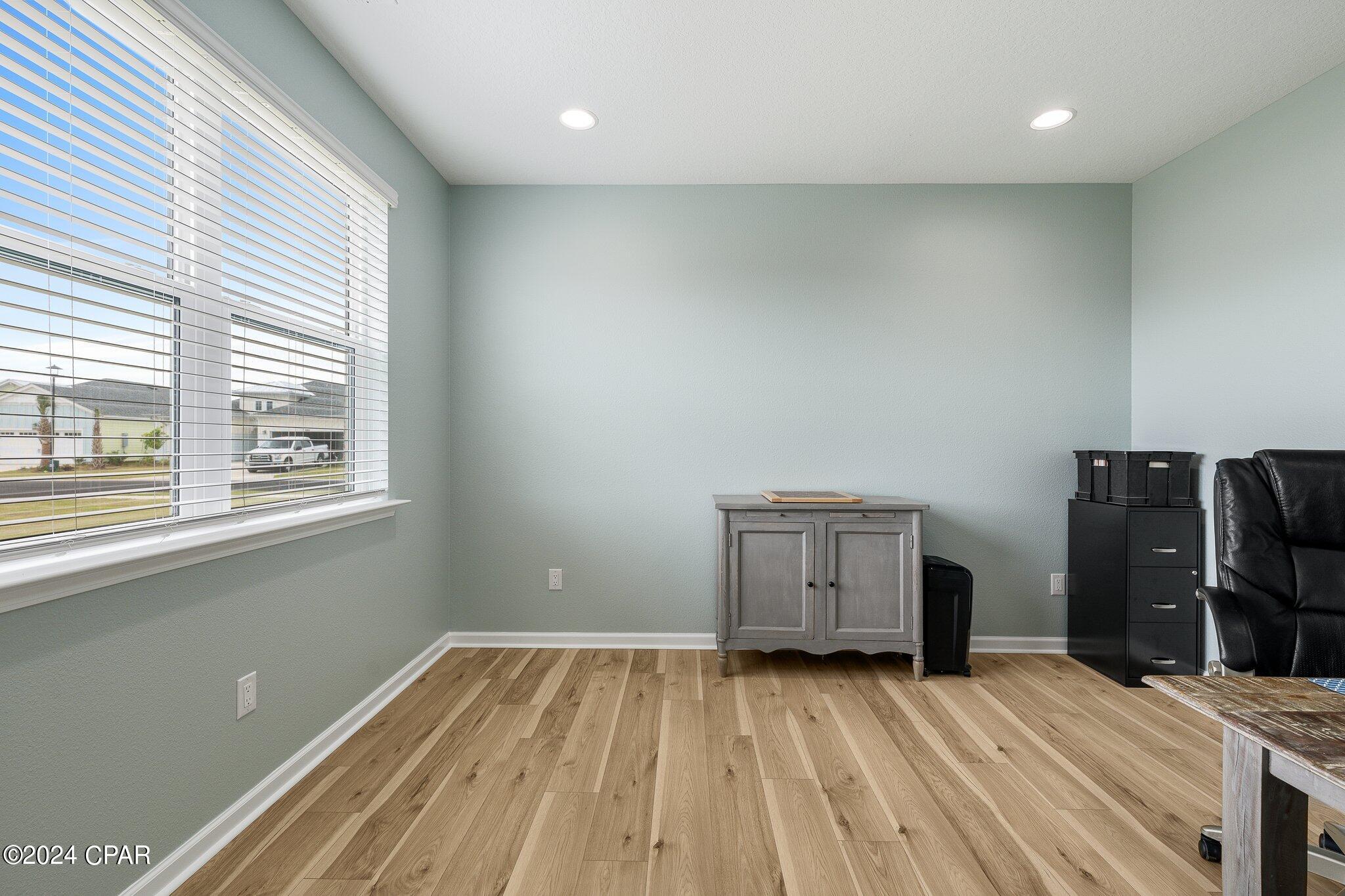 Room with light wood floors, a large window, and a gray cabinet beside an office chair.