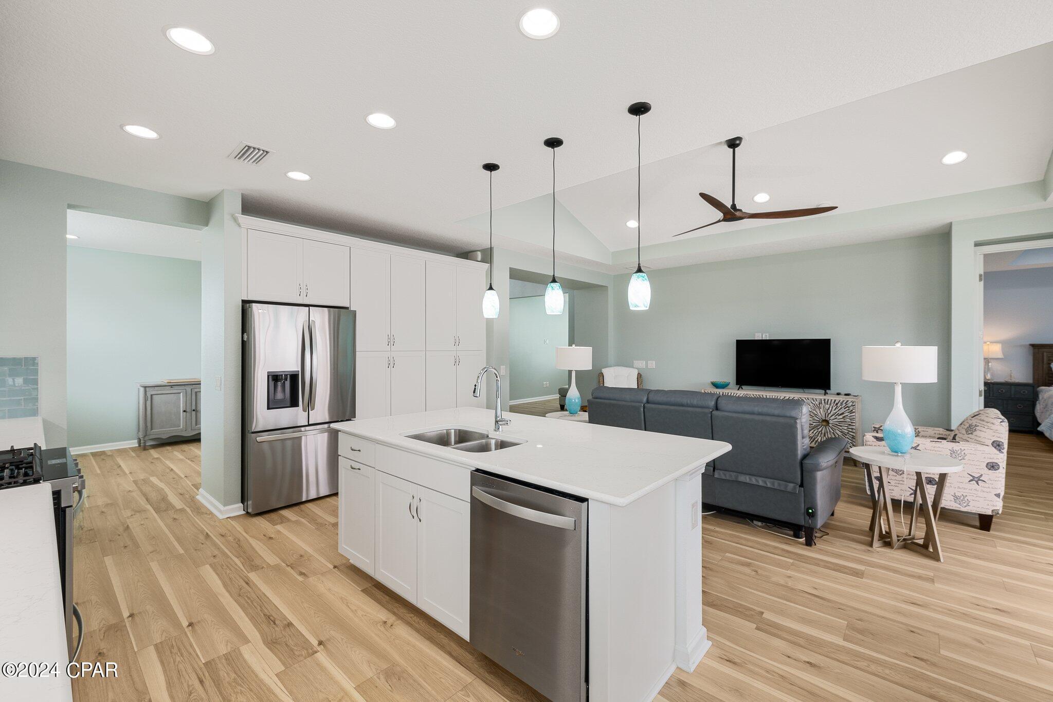Open kitchen with a large white island and stainless appliances adjoining a living room with gray sofa.