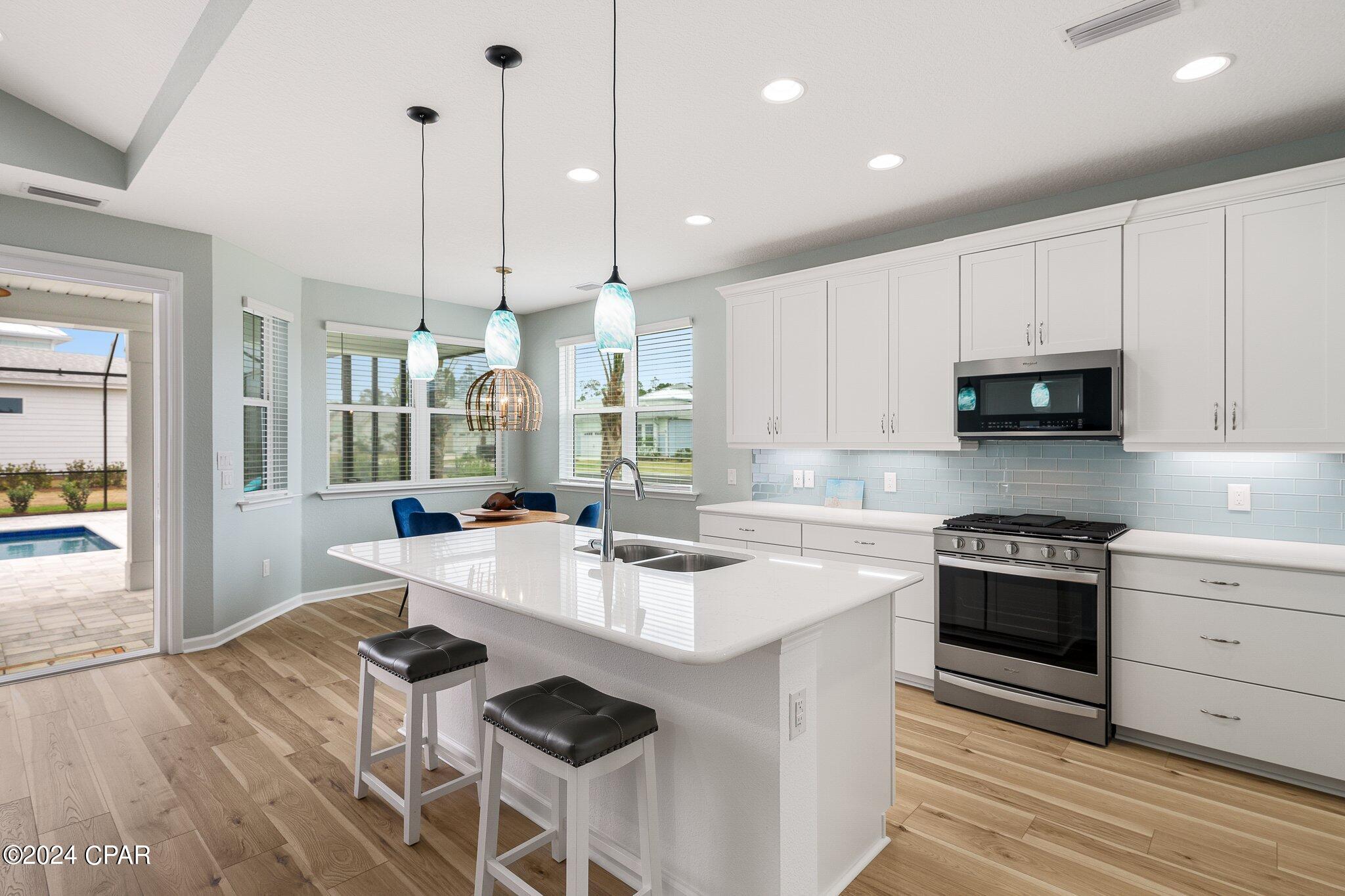Modern kitchen with a large white island, pale blue backsplash, and windows overlooking the patio pool.