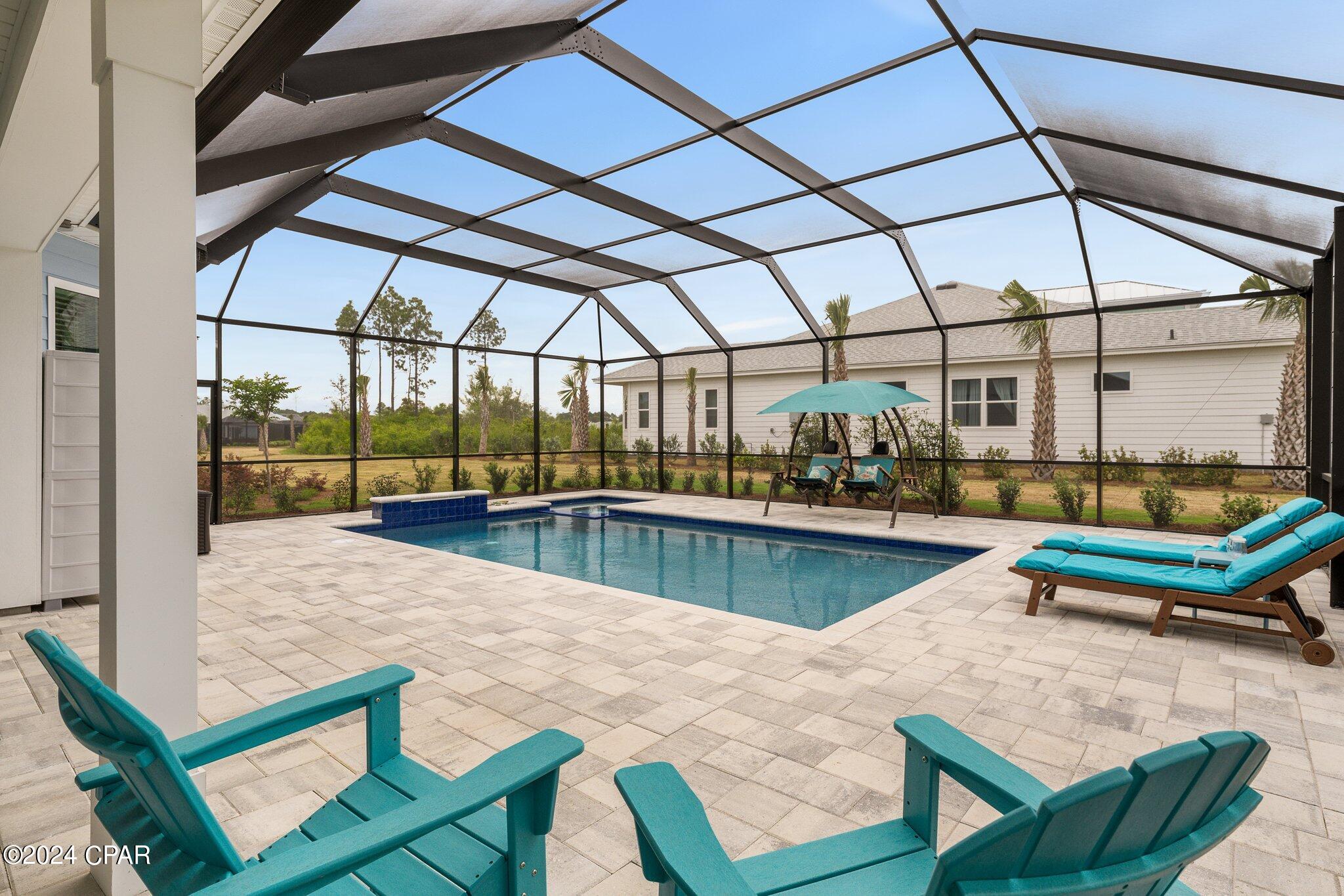 Screened pool patio with turquoise loungers, a hanging swing, and pale stone pavers.