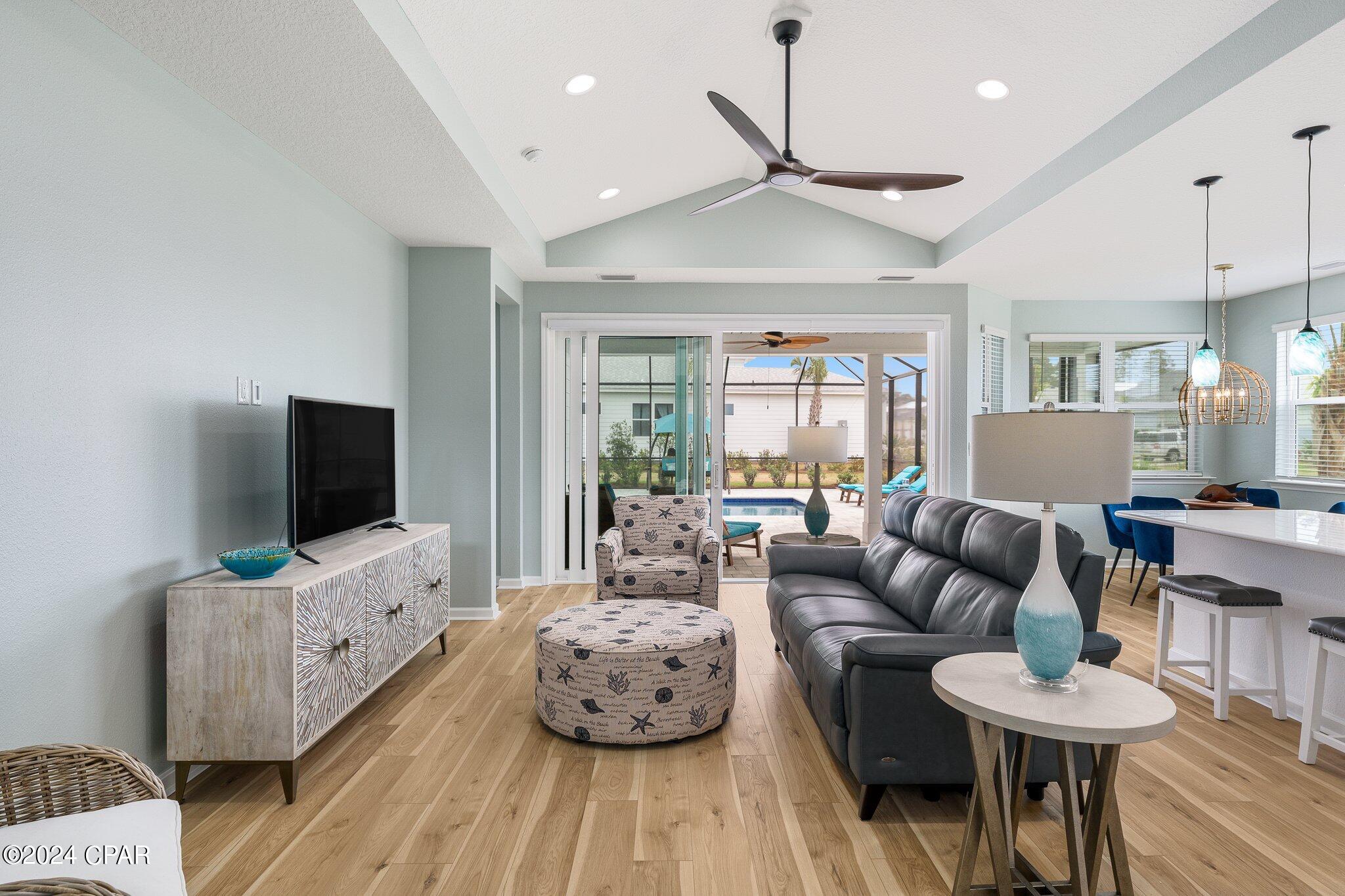 Living room with a gray sectional, vaulted ceiling, and sliding doors overlooking a backyard pool.
