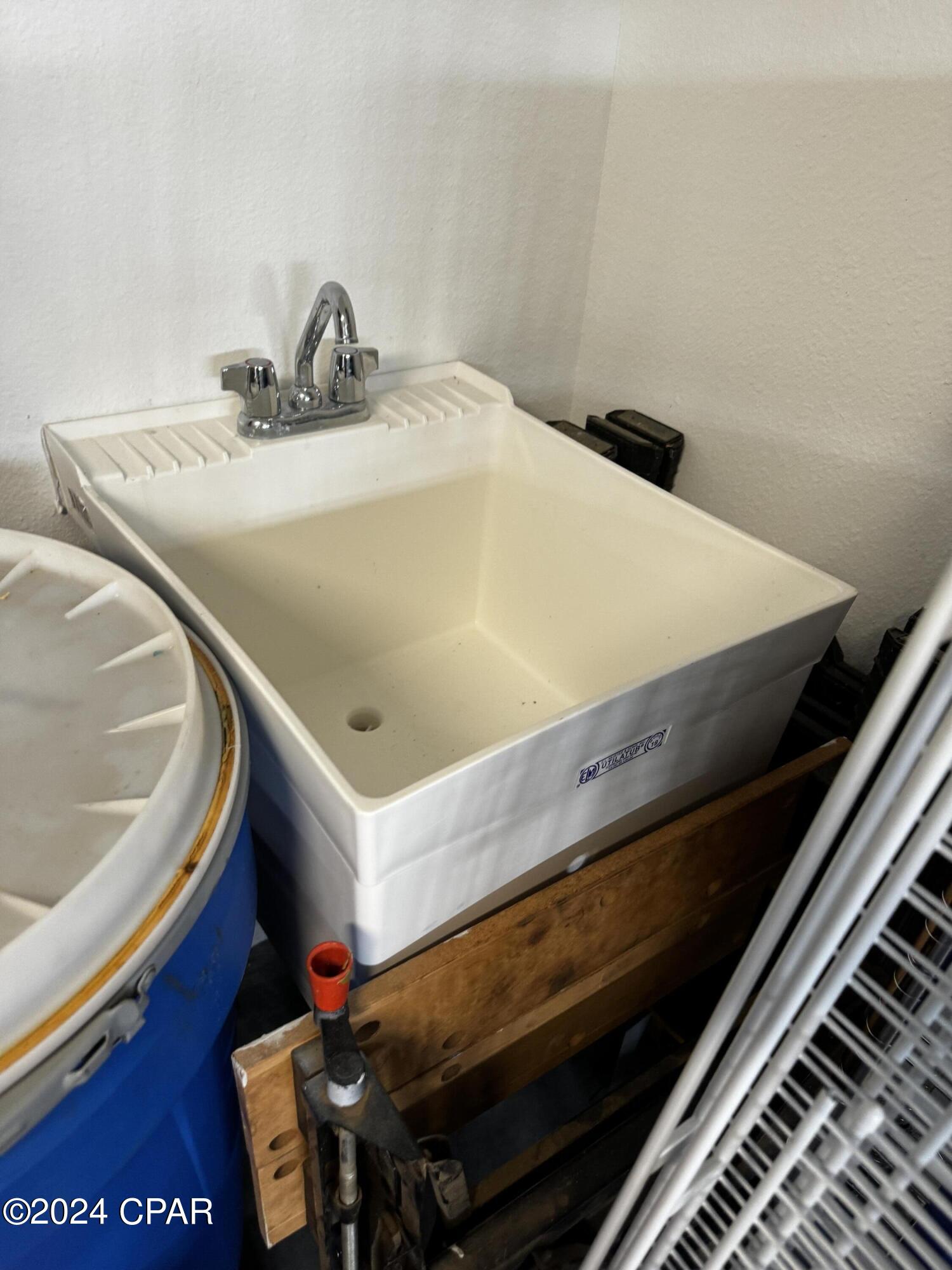 Large white utility sink with chrome faucet beside a blue tank and stored equipment.