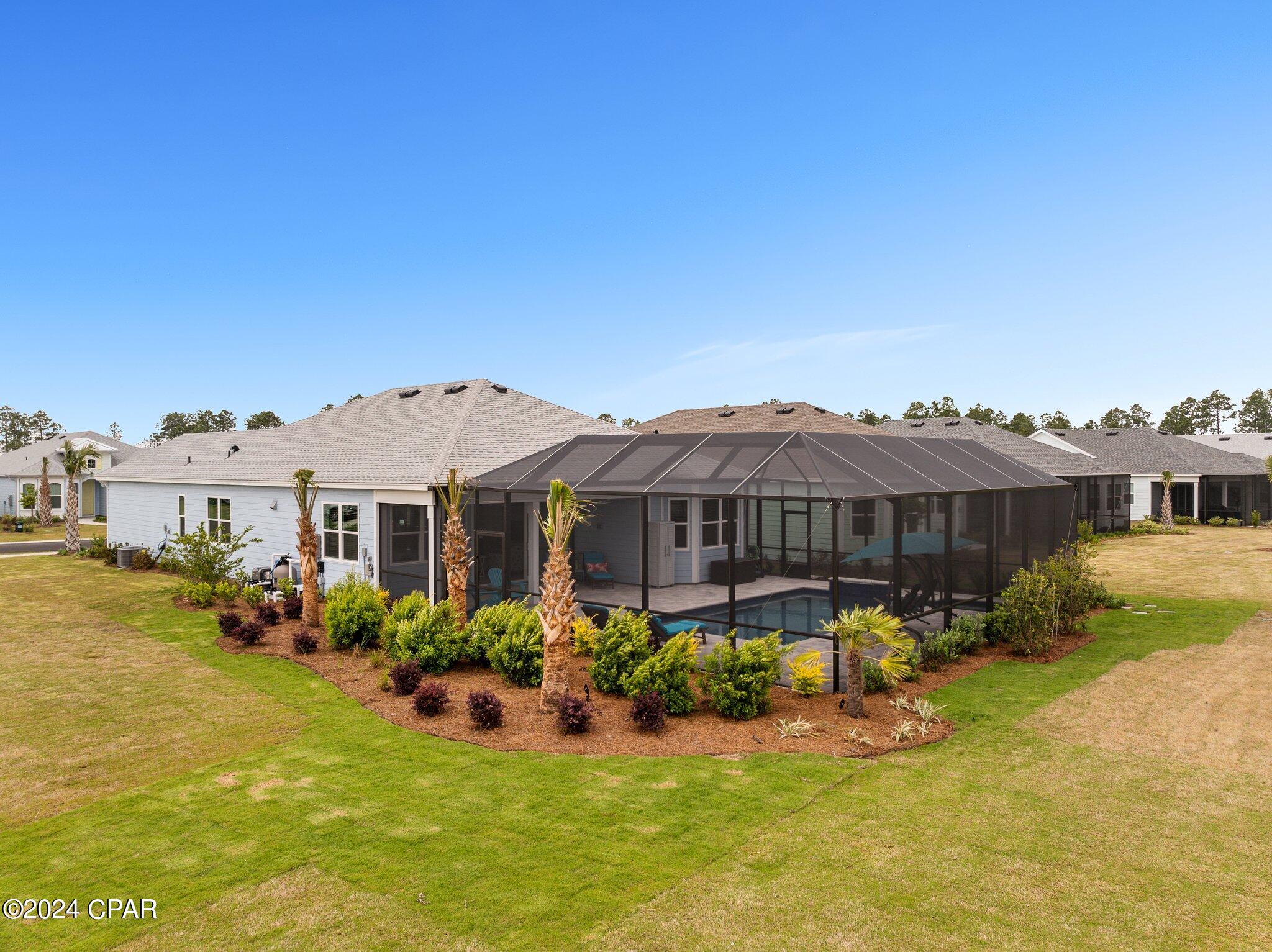 Rear of a single-story home with a large screened pool enclosure and landscaped lawn.