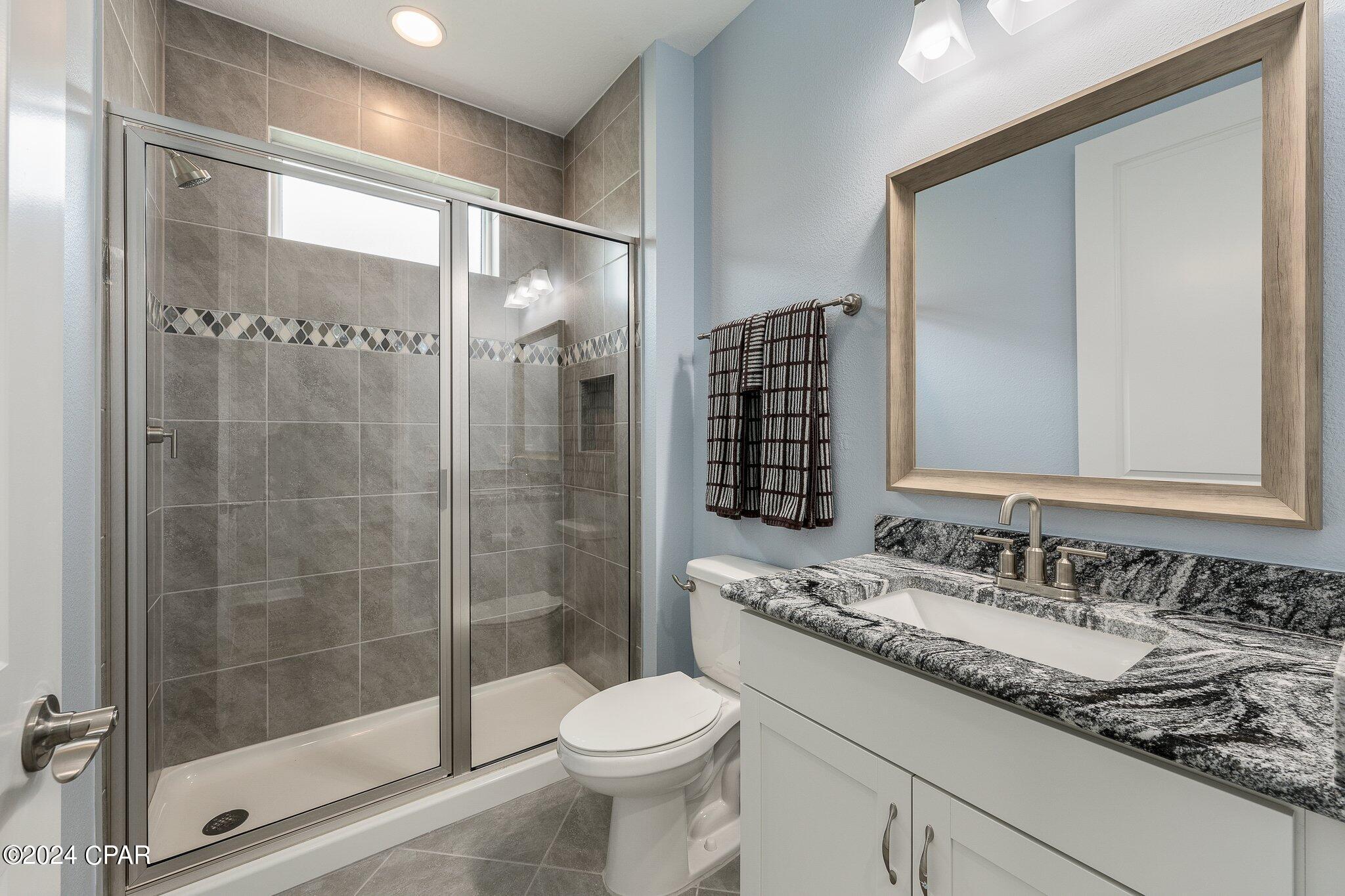 Bathroom with a glass-enclosed gray tile shower and a granite-topped vanity.
