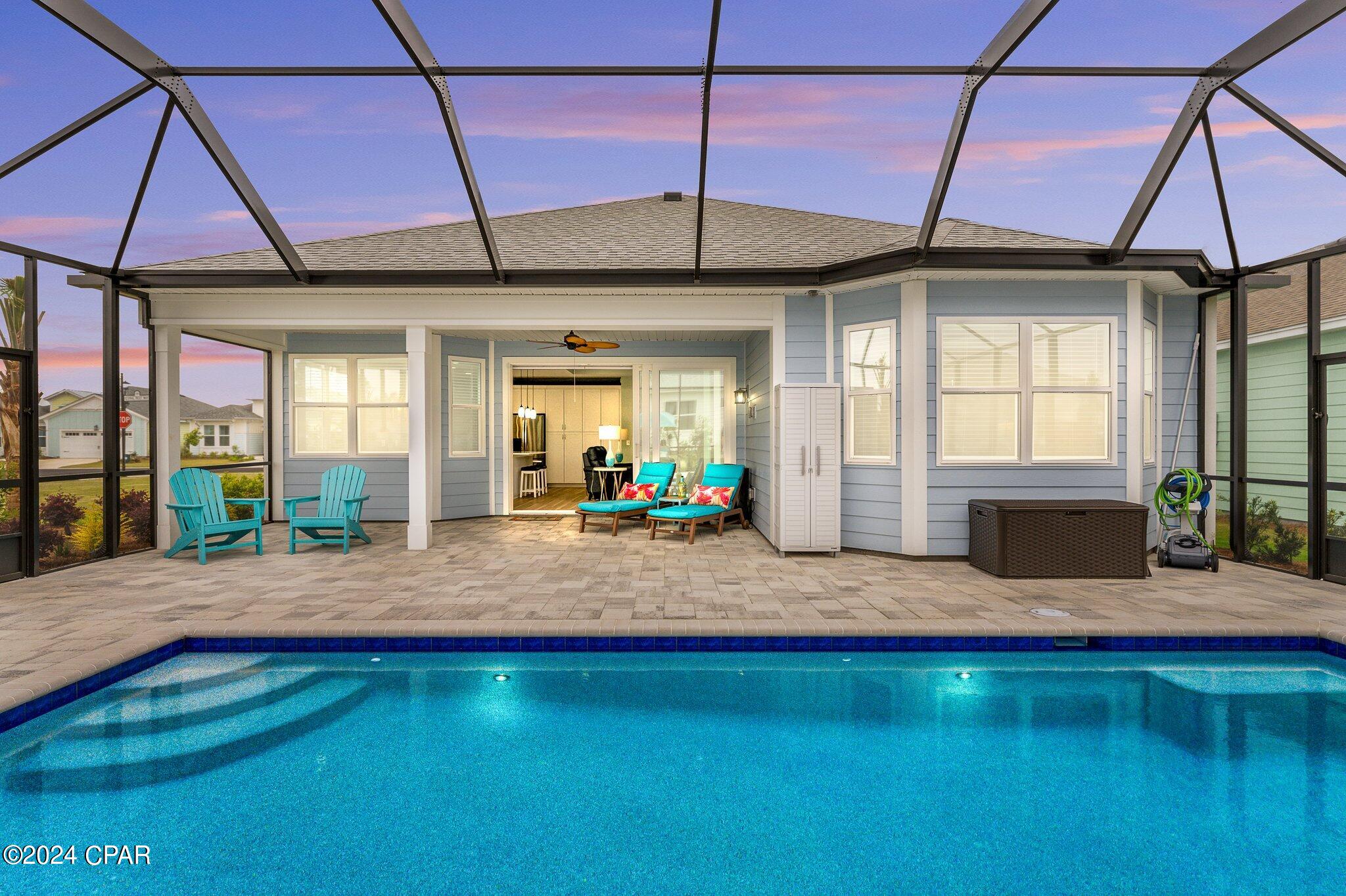 Backyard pool beside a screened patio with turquoise chairs and a blue-sided house.