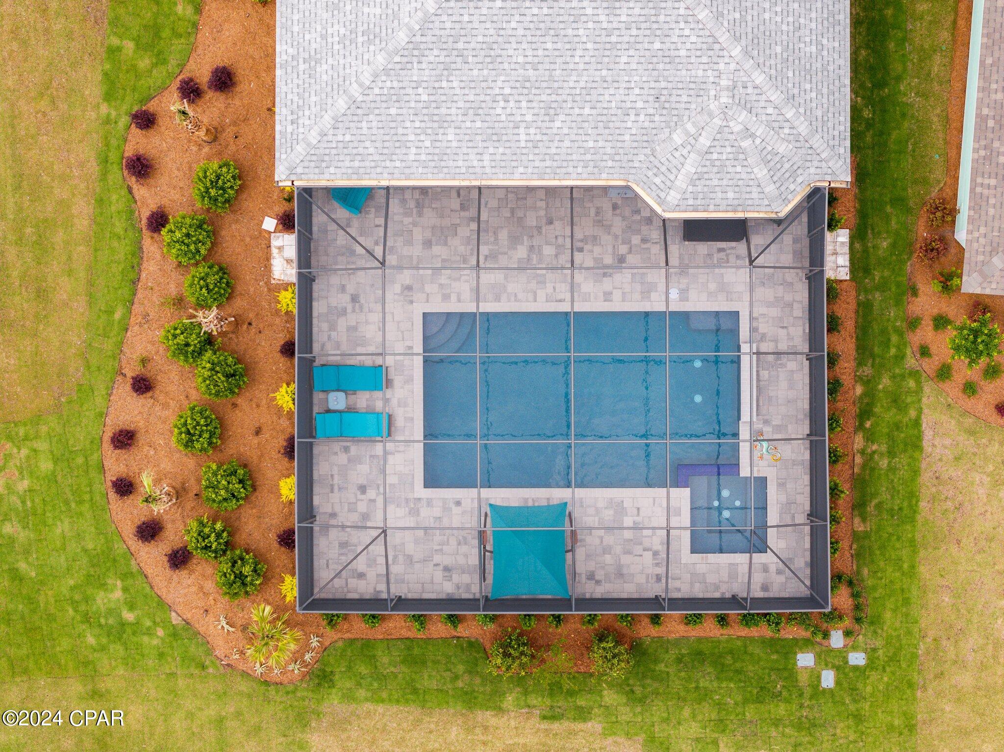 Aerial view of a screened backyard pool and spa with turquoise loungers and landscaped gardens.