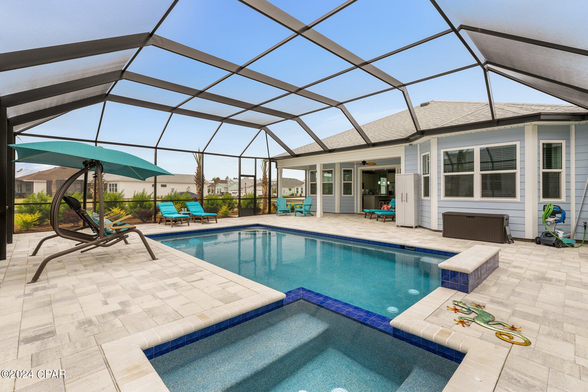 Screened backyard pool and spa beside a light-blue house, with turquoise lounge chairs and a hanging chair.